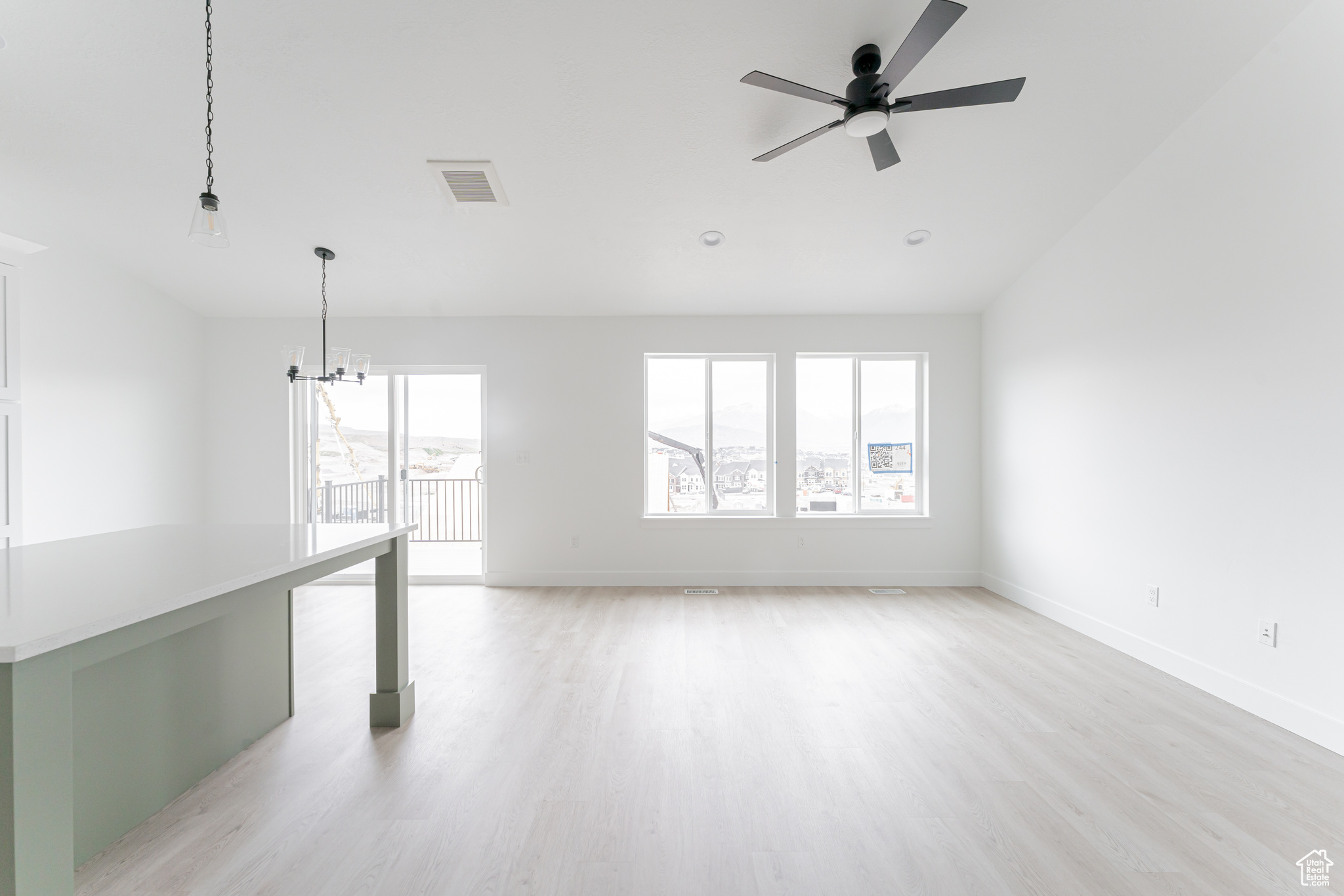 Spare room with plenty of natural light, light wood-type flooring, and ceiling fan with notable chandelier