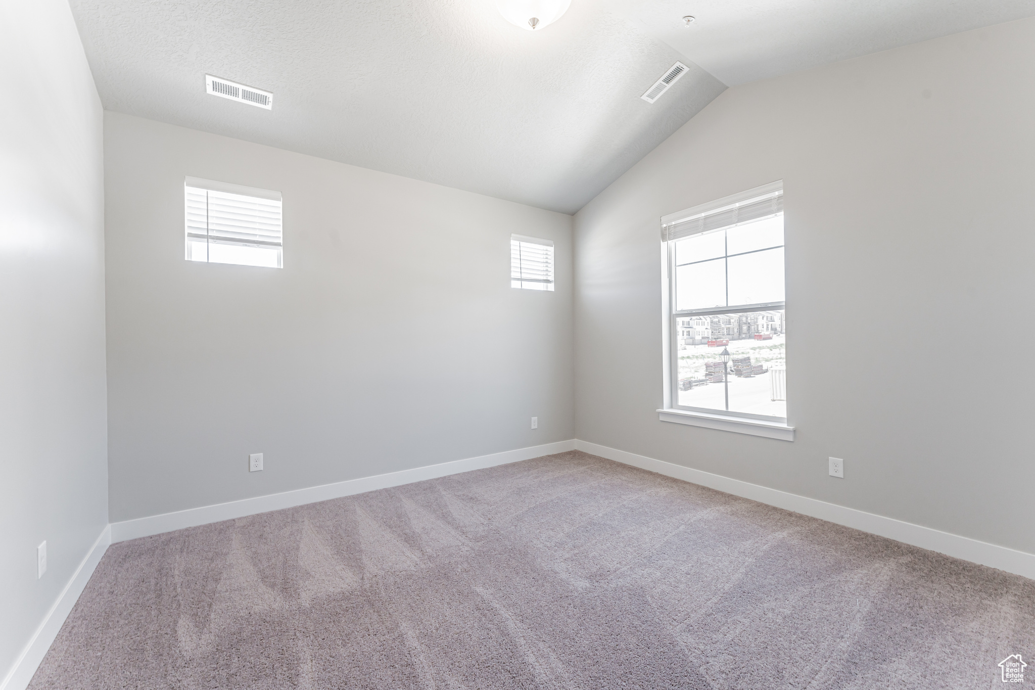 Spare room featuring carpet, a wealth of natural light, and lofted ceiling