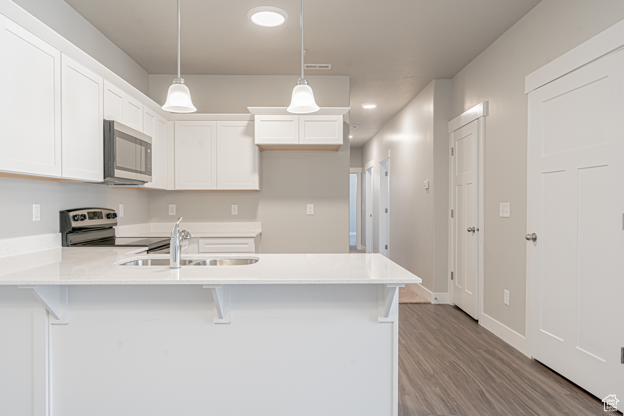 Kitchen featuring decorative light fixtures, hardwood / wood-style flooring, white cabinets, sink, and electric range oven