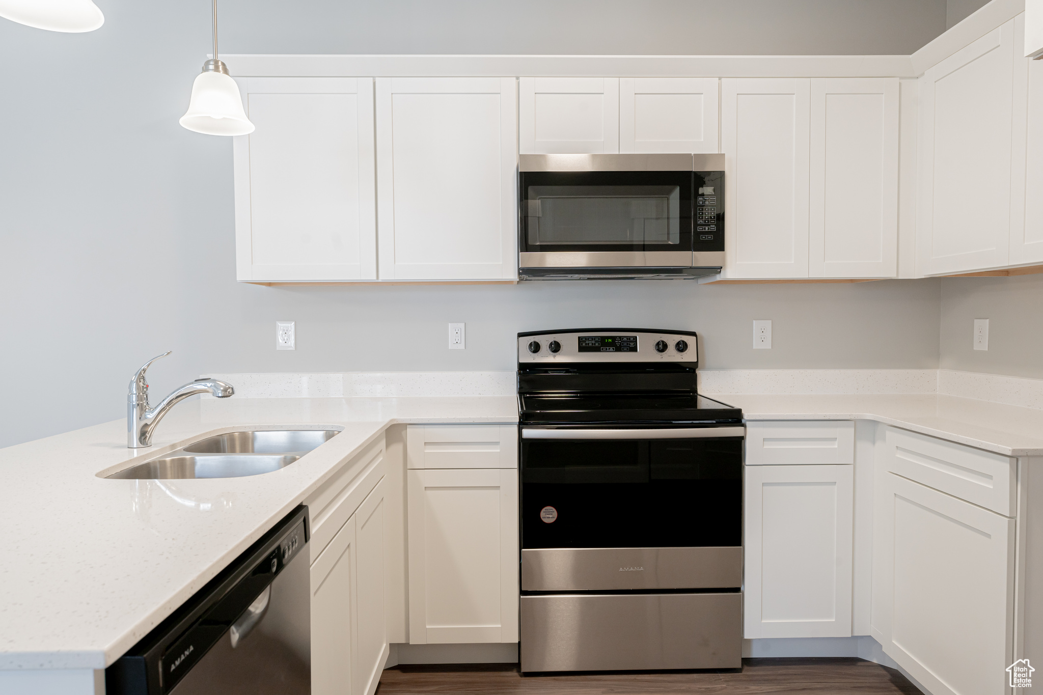 Kitchen with white cabinets, hanging light fixtures, appliances with stainless steel finishes, wood-type flooring, and sink