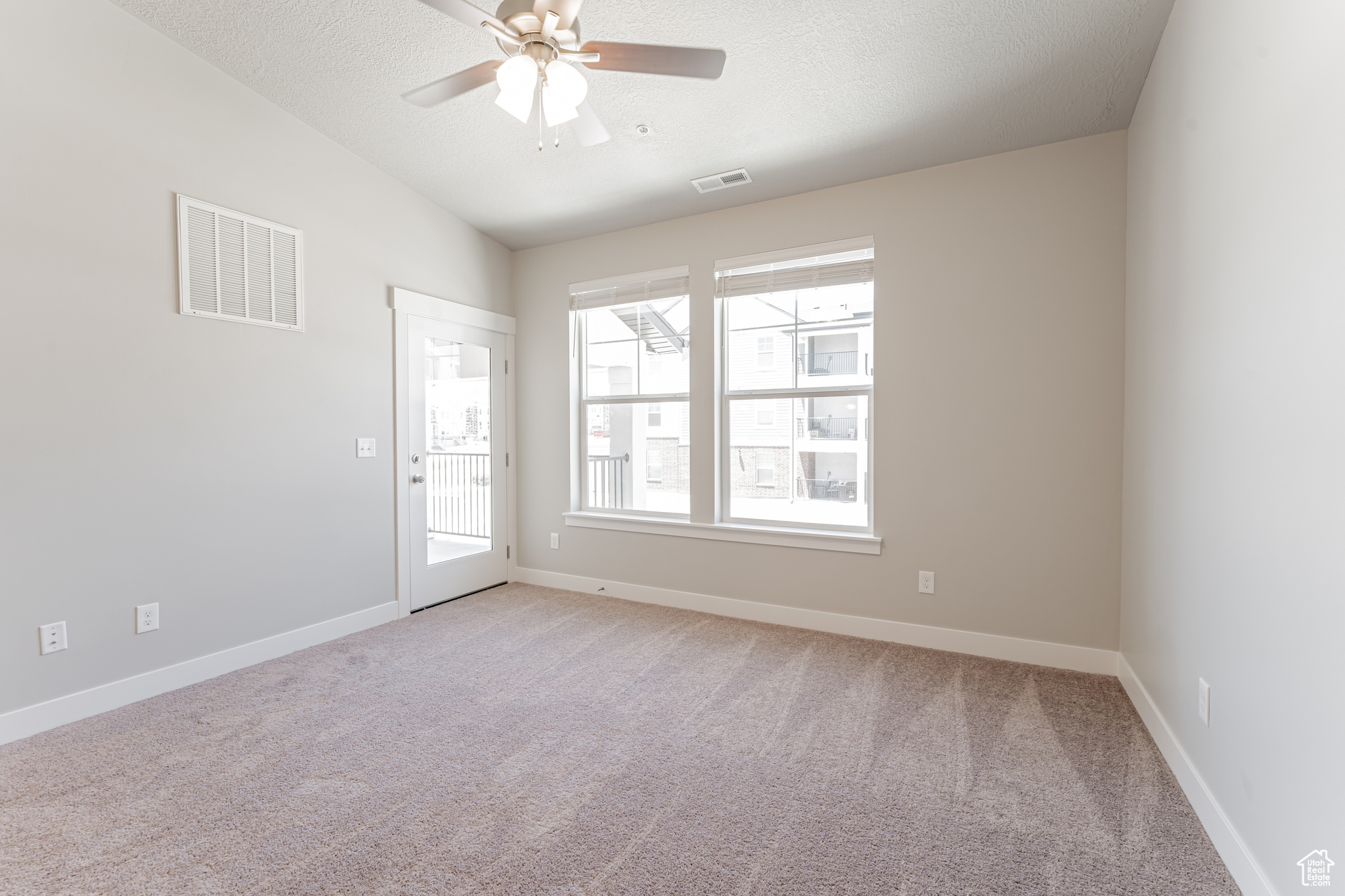 Carpeted spare room featuring a textured ceiling, a wealth of natural light, and ceiling fan