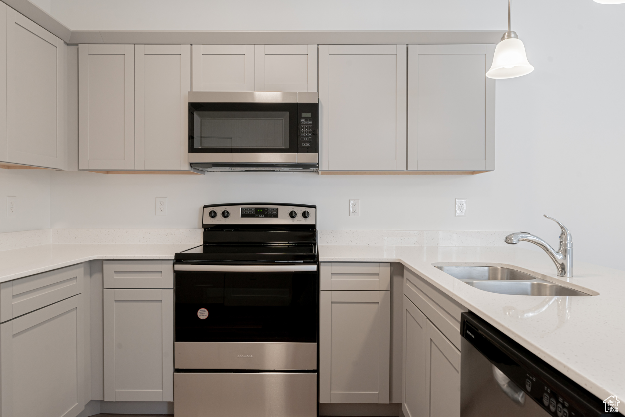 Kitchen with gray cabinetry, light stone counters, stainless steel appliances, and sink