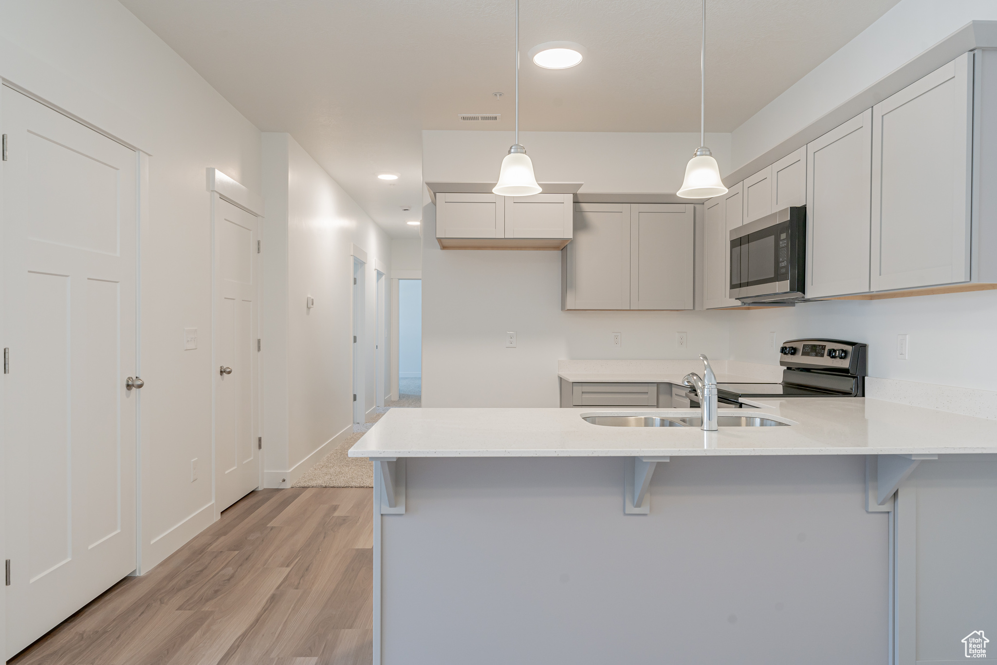 Kitchen with kitchen peninsula, pendant lighting, range with electric stovetop, light hardwood / wood-style floors, and sink