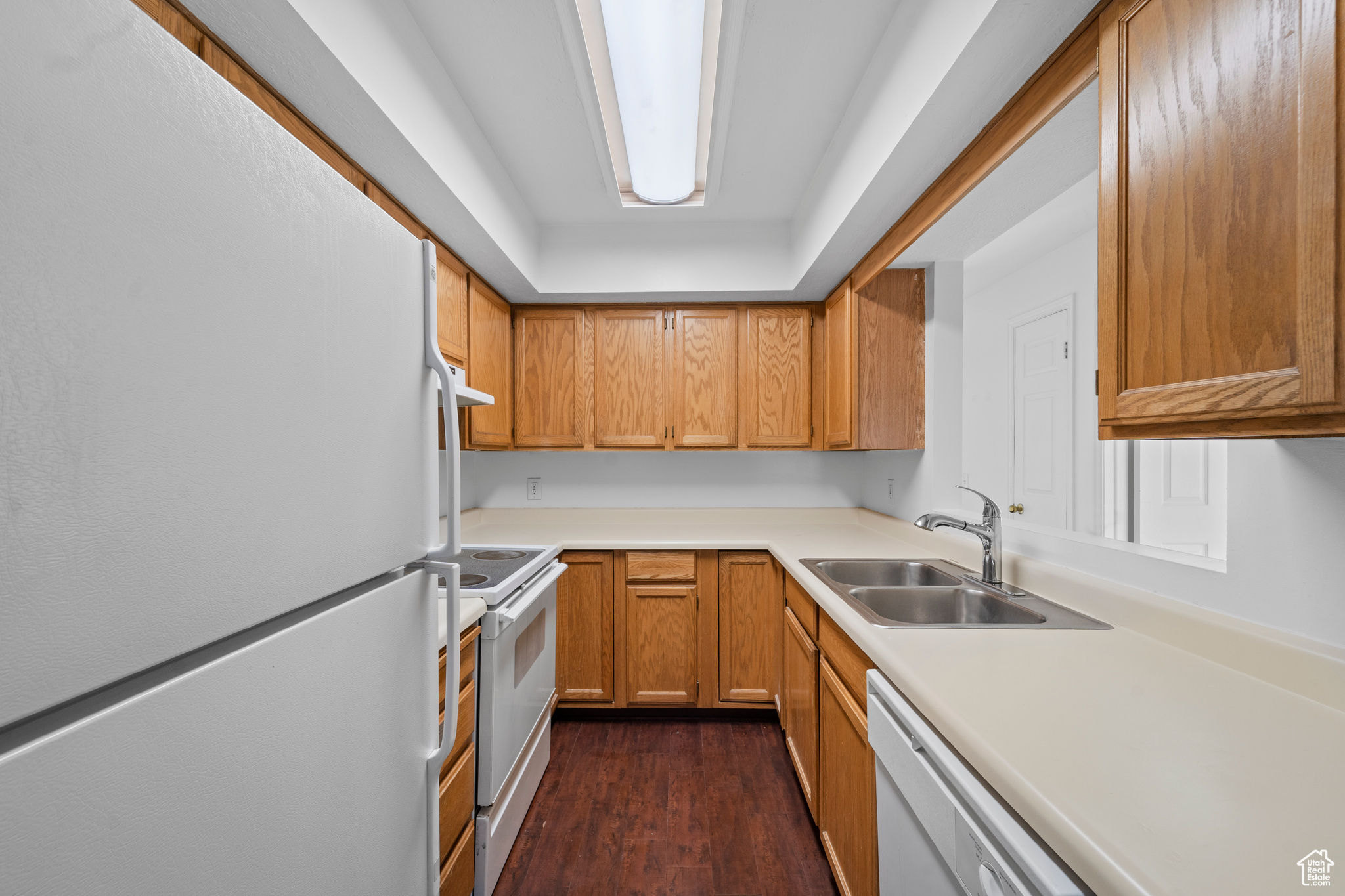 Kitchen with white appliances, dark hardwood-type laminate flooring, and sink