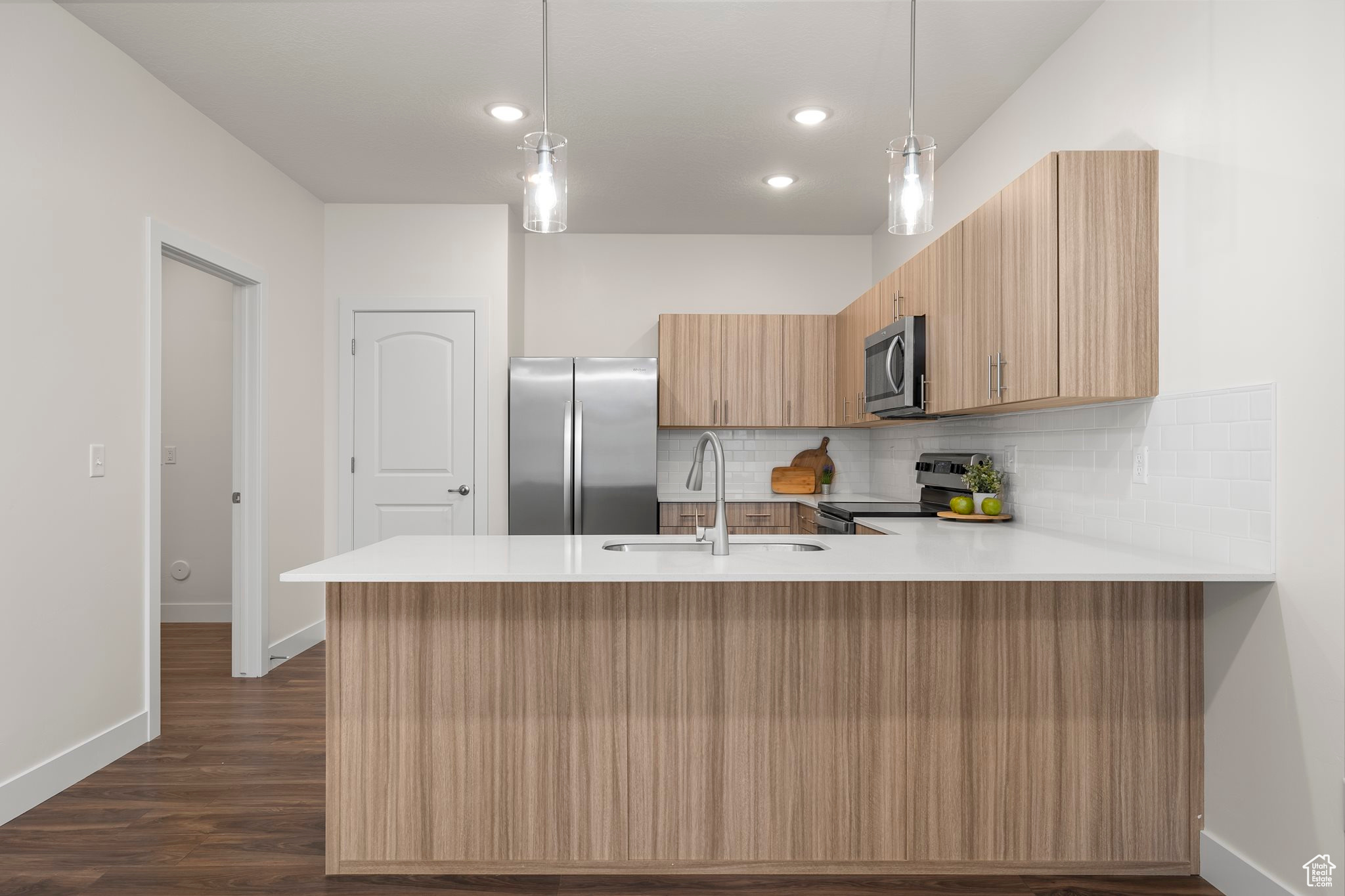 Kitchen with dark wood-type flooring, hanging light fixtures, stainless steel appliances, and sink