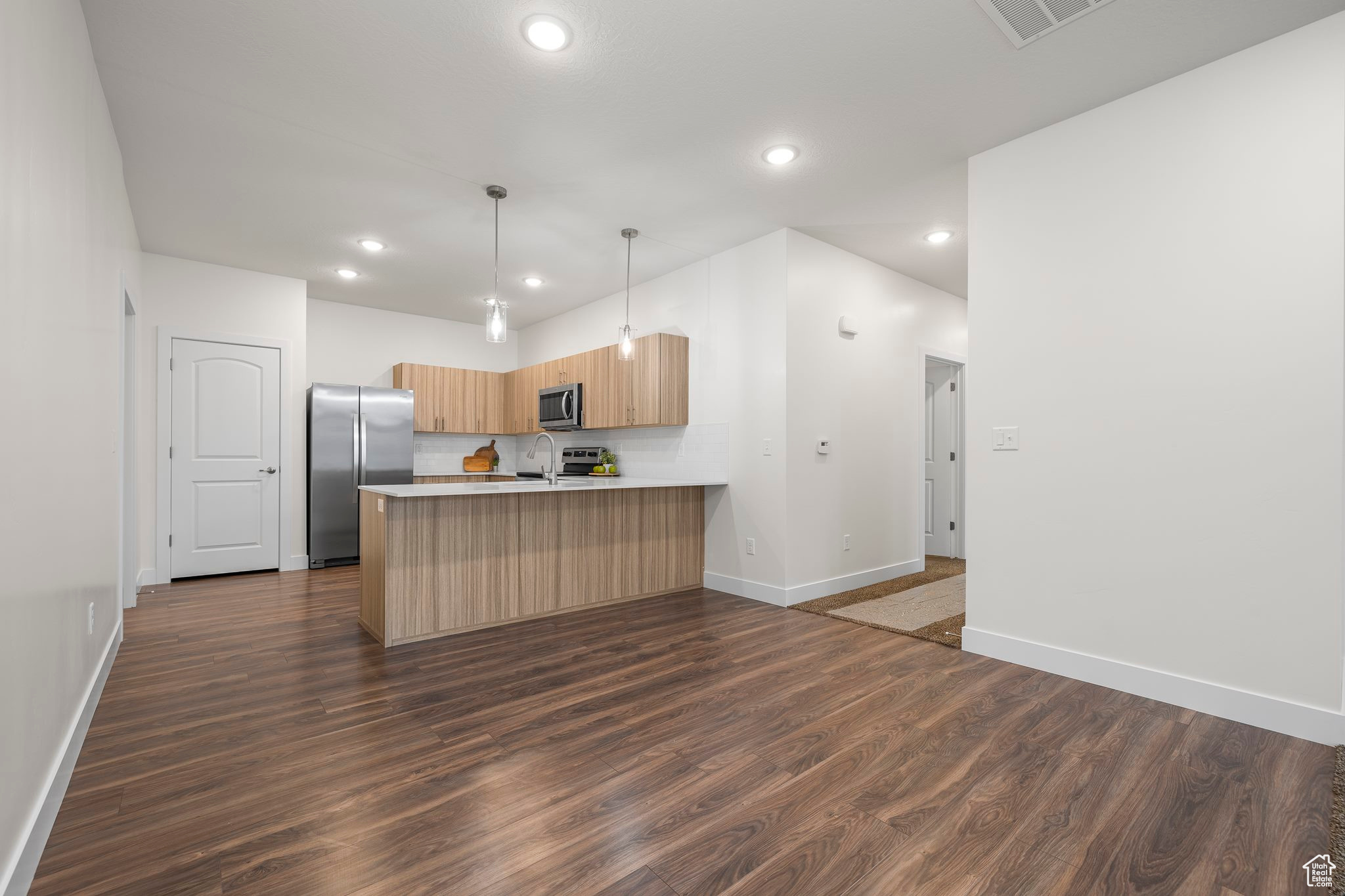 Kitchen featuring kitchen peninsula, dark wood-type flooring, stainless steel appliances, and decorative light fixtures