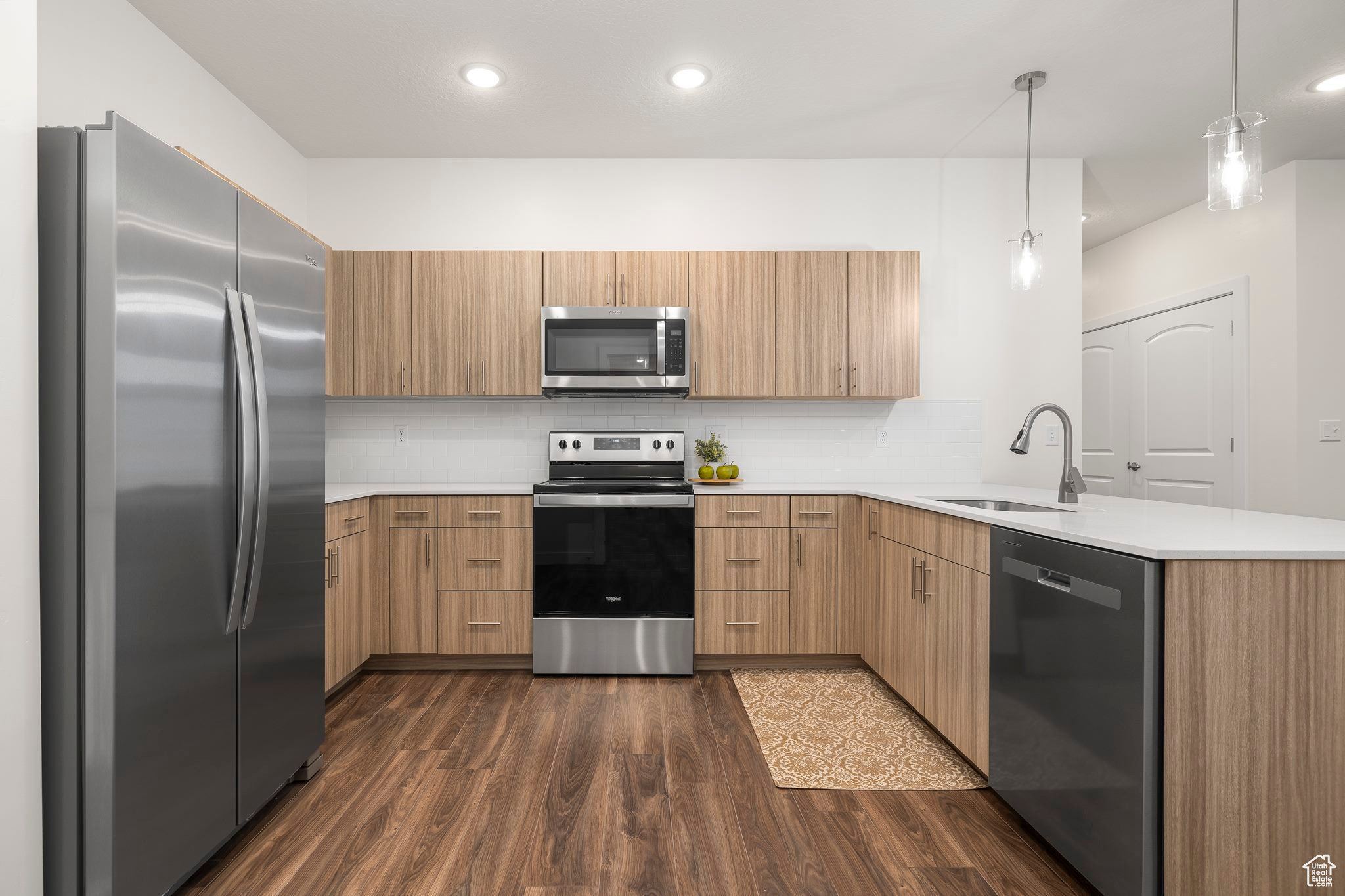 Kitchen featuring sink, dark hardwood / wood-style flooring, kitchen peninsula, decorative light fixtures, and appliances with stainless steel finishes