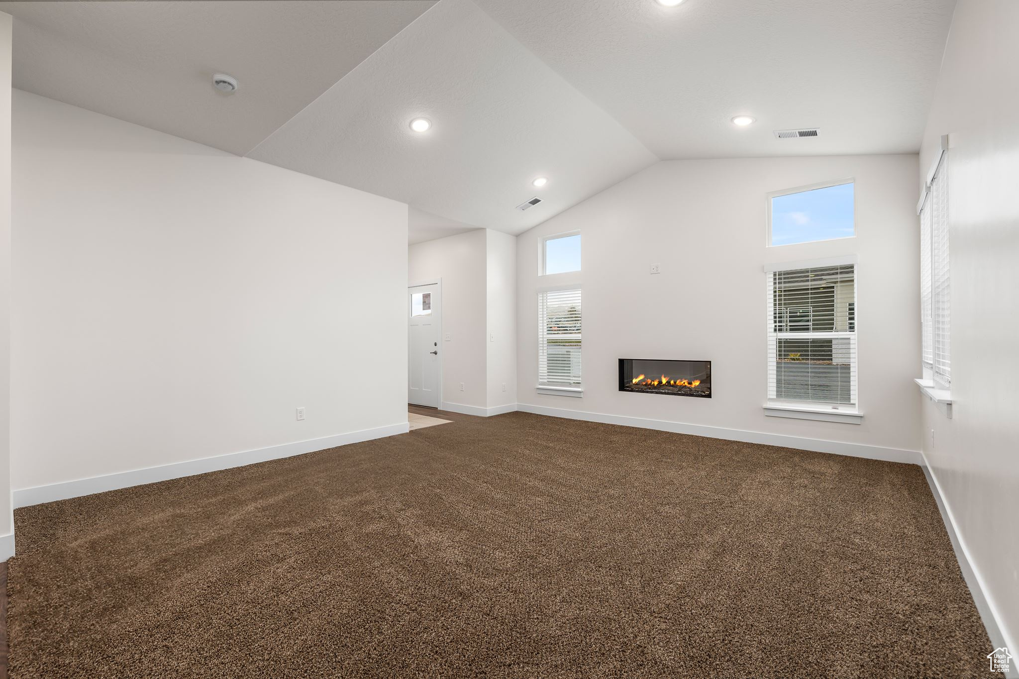 Unfurnished living room with vaulted ceiling and dark colored carpet