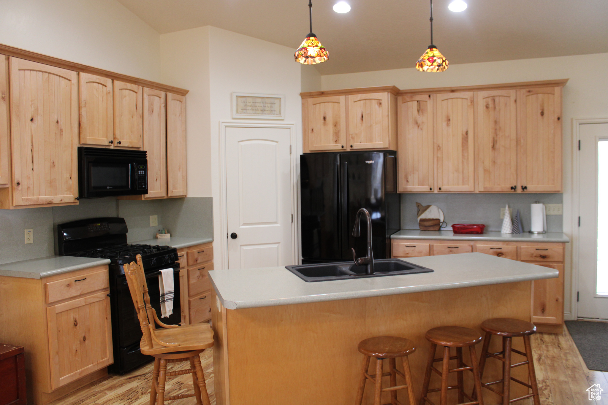 Kitchen with a center island with sink, light hardwood / wood-style floors, black appliances, and a breakfast bar