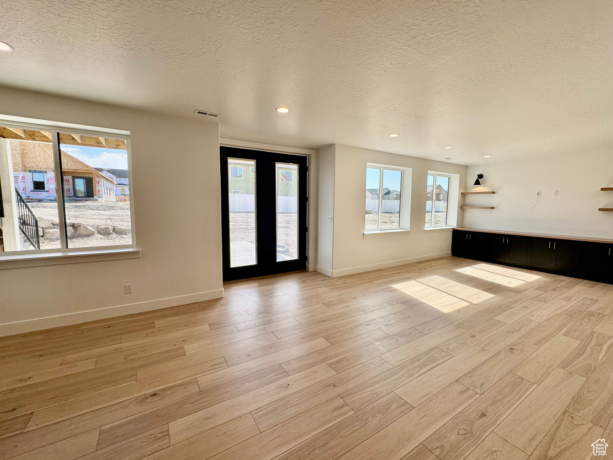 Unfurnished room featuring a textured ceiling, light hardwood / wood-style flooring, and french doors