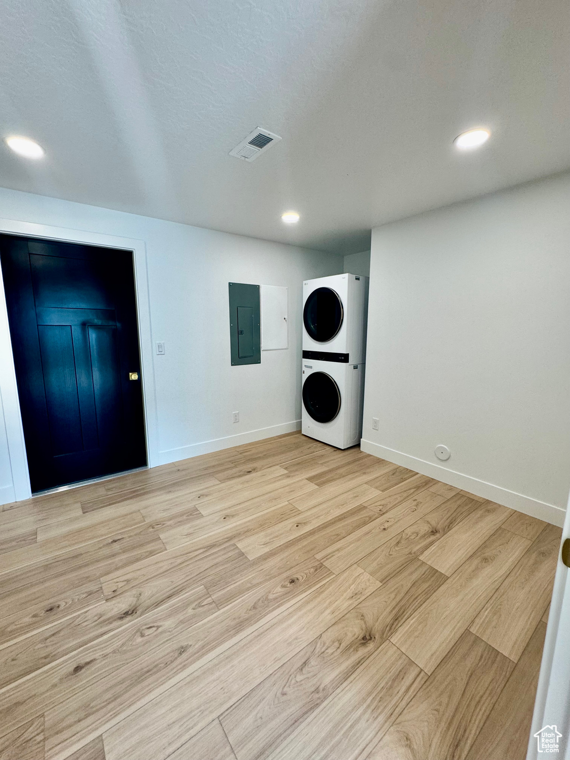 Laundry area featuring electric panel, light hardwood / wood-style flooring, and stacked washer / dryer