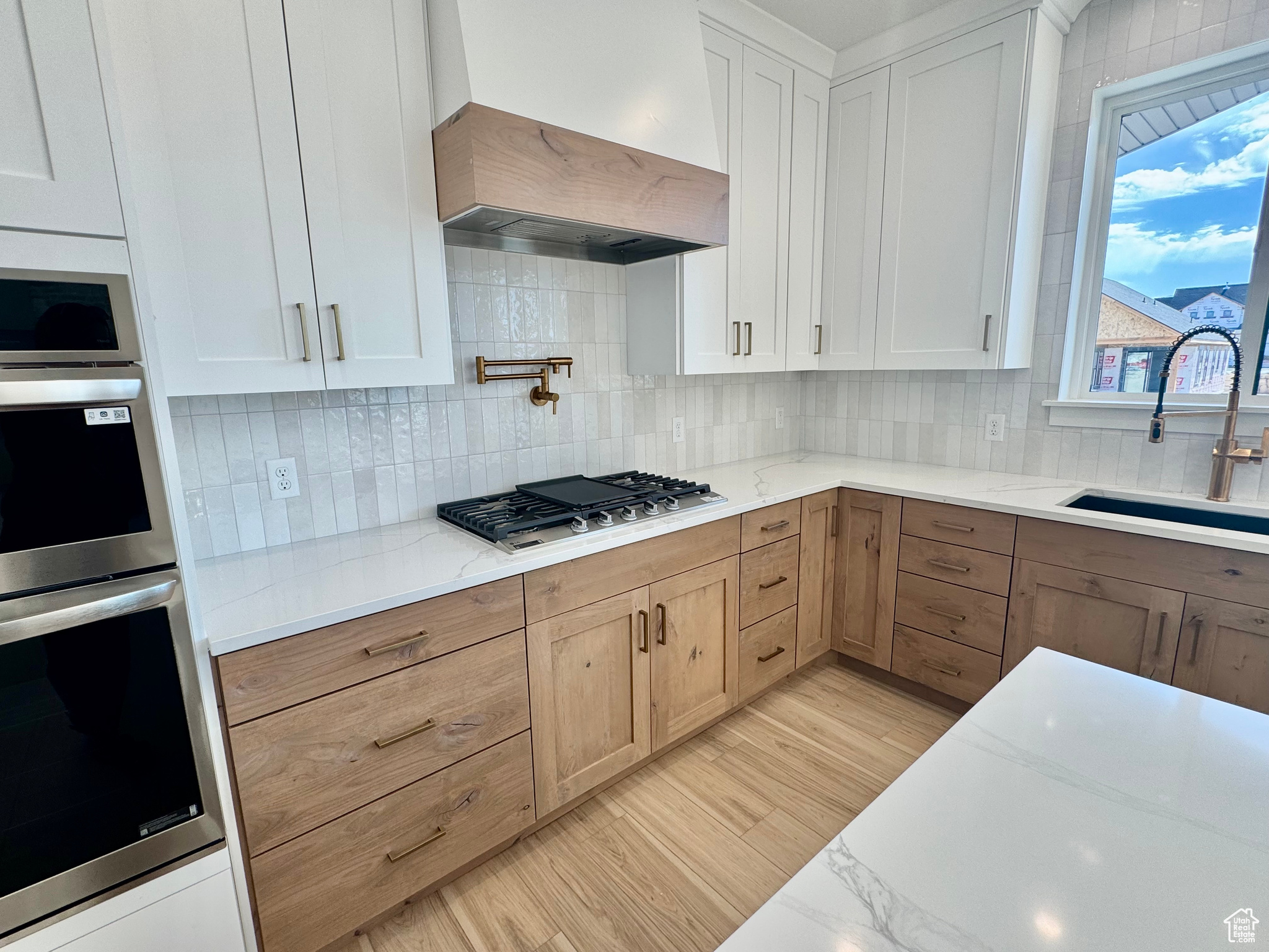 Kitchen featuring sink, white cabinetry, custom exhaust hood, decorative backsplash, and appliances with stainless steel finishes