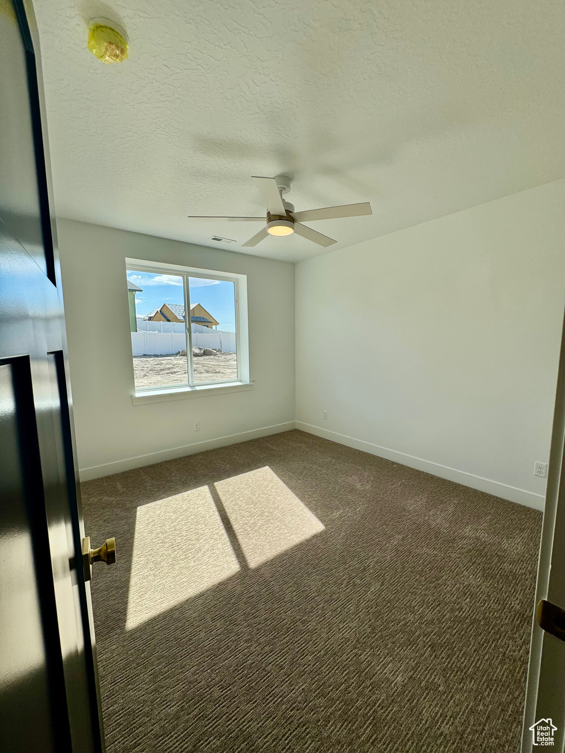 Unfurnished room with dark carpet, ceiling fan, and a textured ceiling