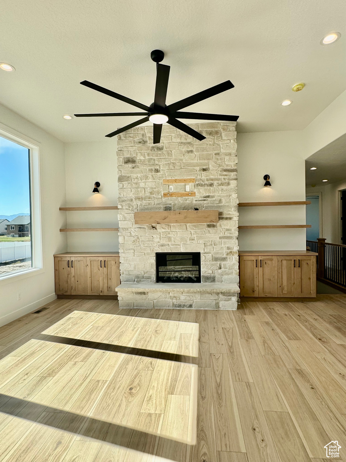 Unfurnished living room featuring light wood-type flooring, a stone fireplace, and ceiling fan