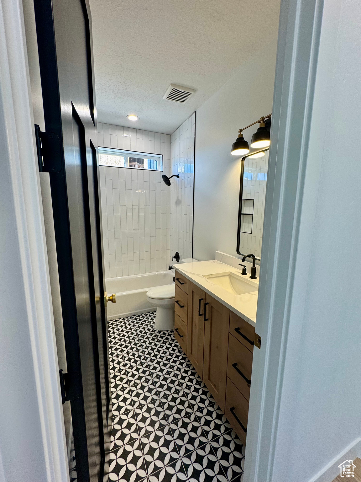 Full bathroom with a textured ceiling, tile patterned floors, vanity, tiled shower / bath, and toilet