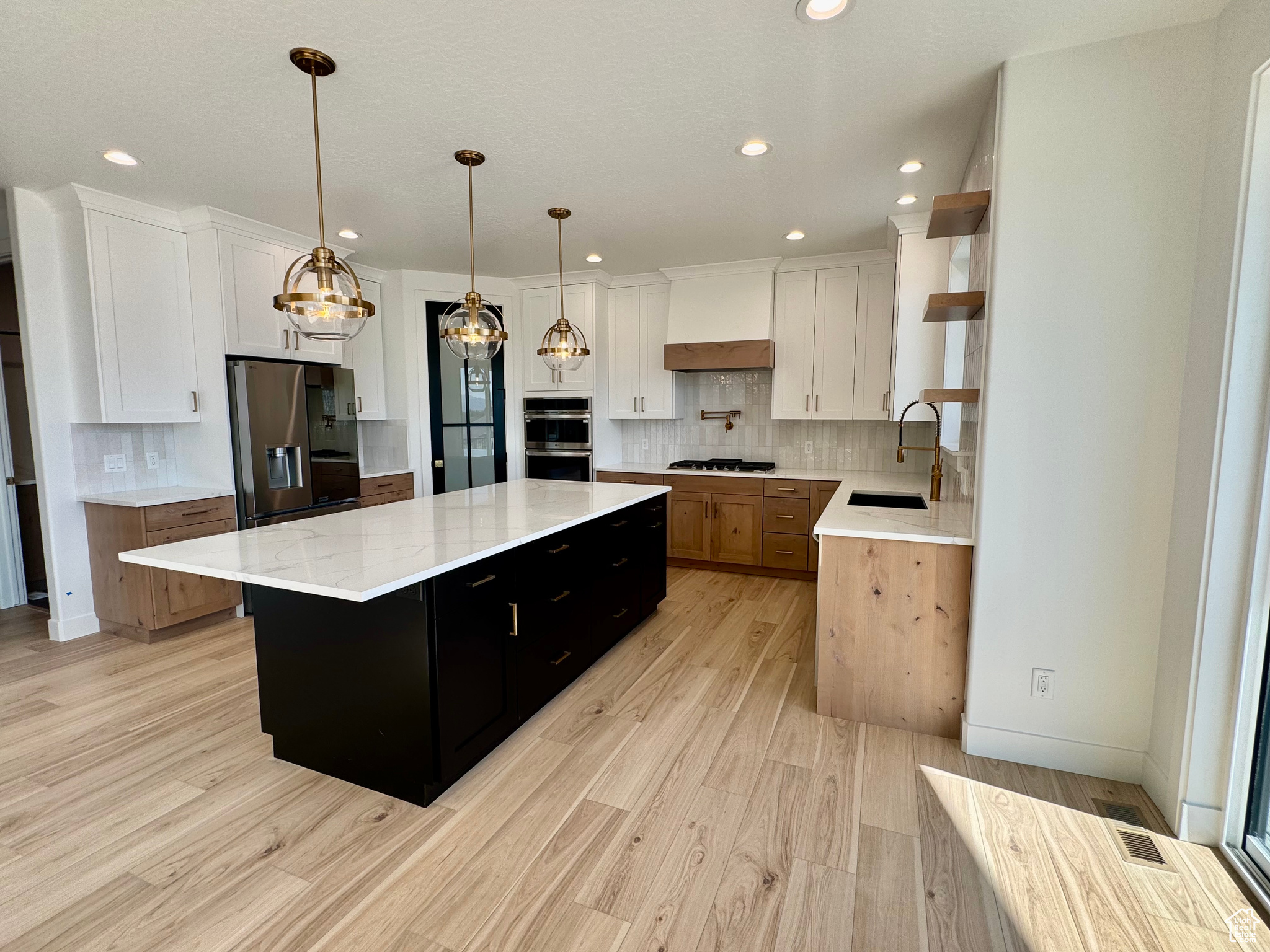 Kitchen featuring white cabinets, a large island, stainless steel appliances, and hanging light fixtures