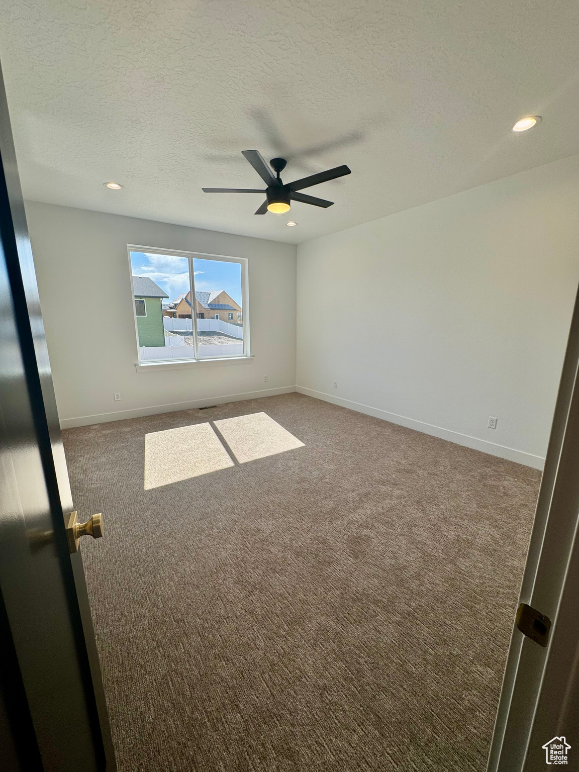 Empty room featuring ceiling fan, a textured ceiling, and carpet