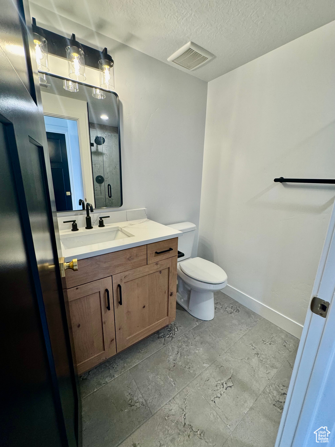 Bathroom with a textured ceiling, a shower, vanity, and toilet