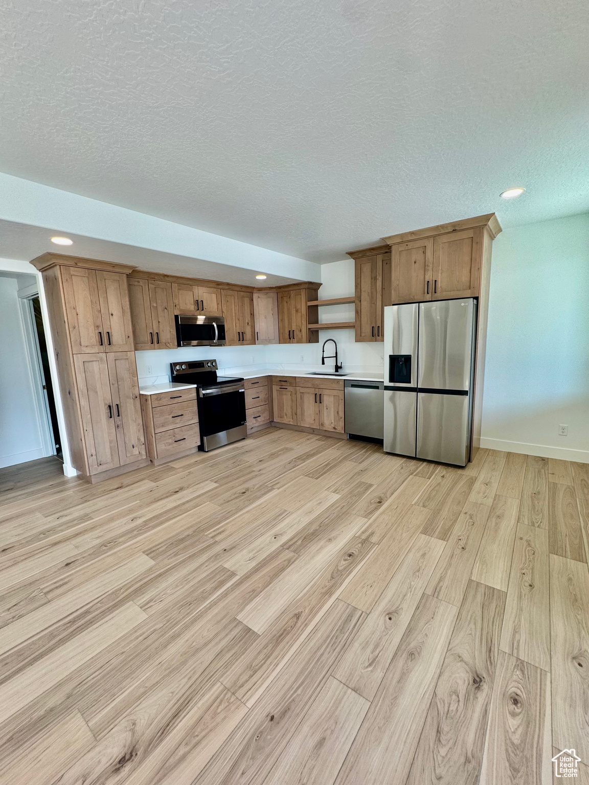 Kitchen featuring sink, stainless steel appliances, light hardwood / wood-style floors, and a textured ceiling