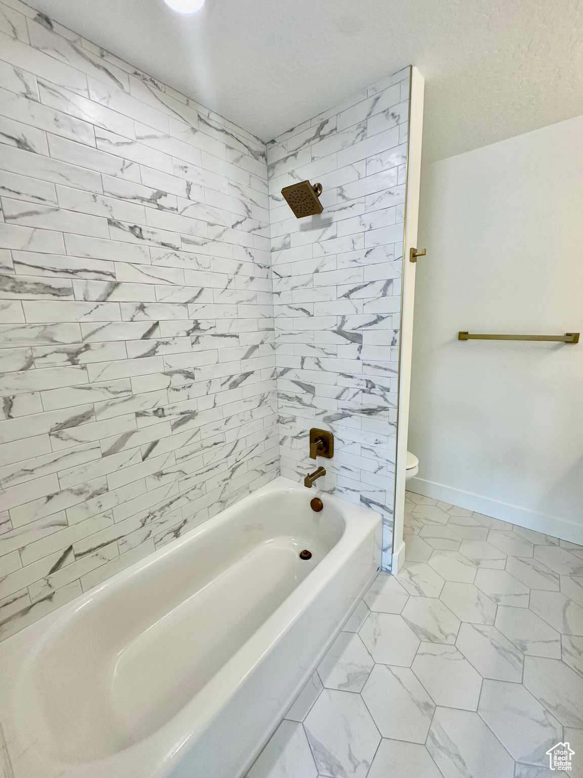 Bathroom with a textured ceiling, tiled shower / bath combo, and toilet