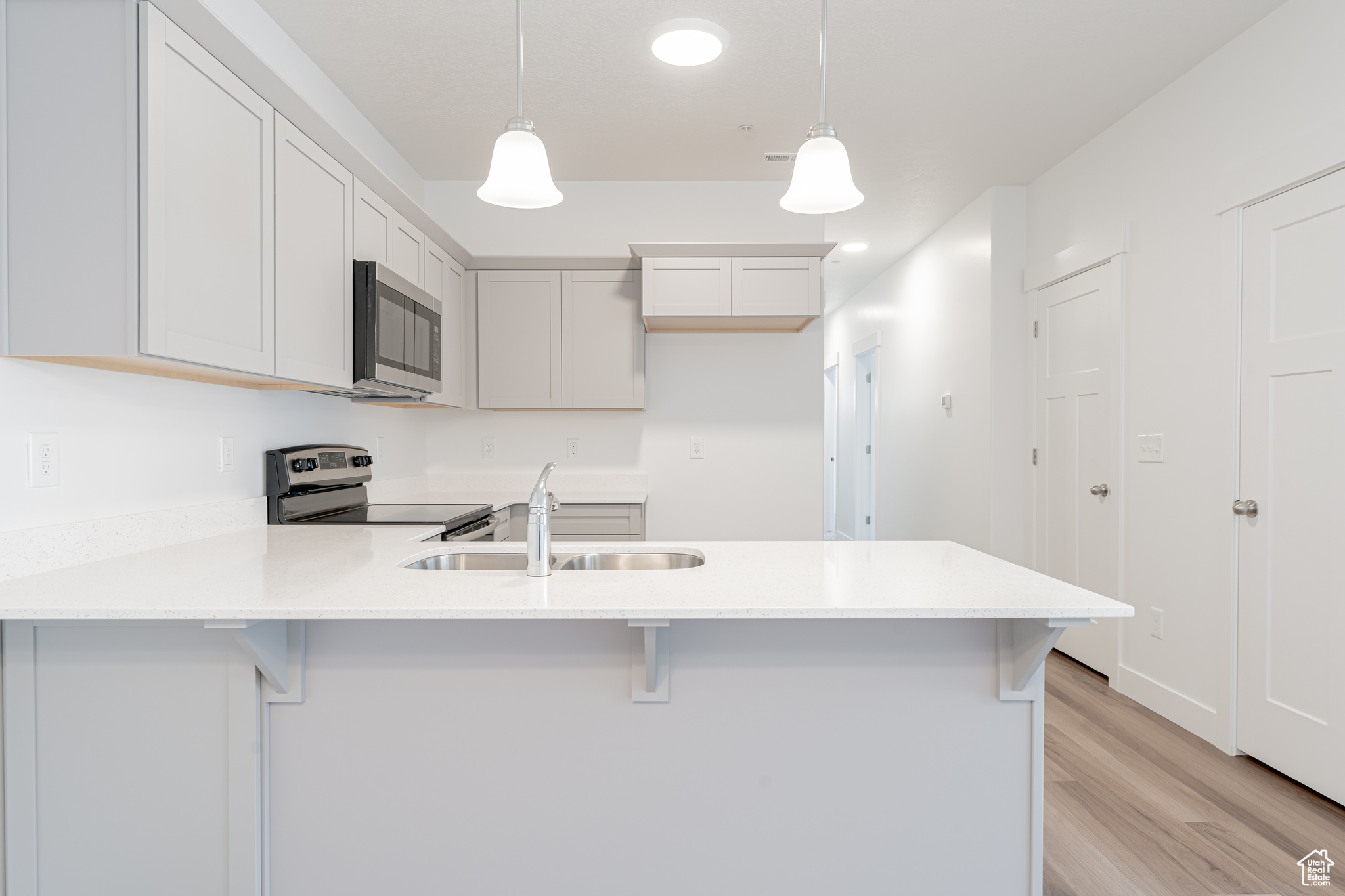 Kitchen with a kitchen bar, hanging light fixtures, appliances with stainless steel finishes, and white cabinets