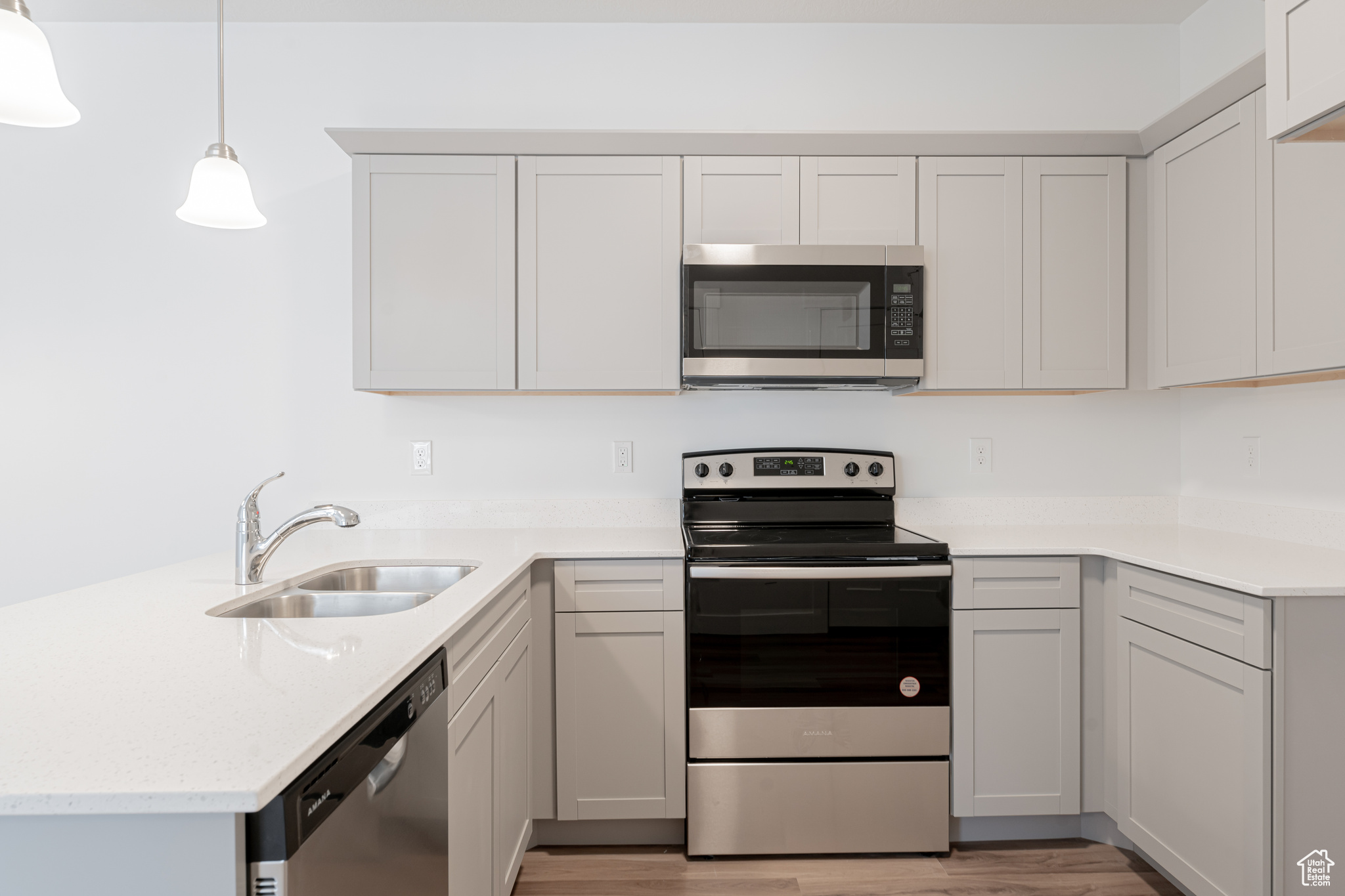 Kitchen featuring decorative light fixtures, sink, appliances with stainless steel finishes, white cabinets, and light hardwood / wood-style floors