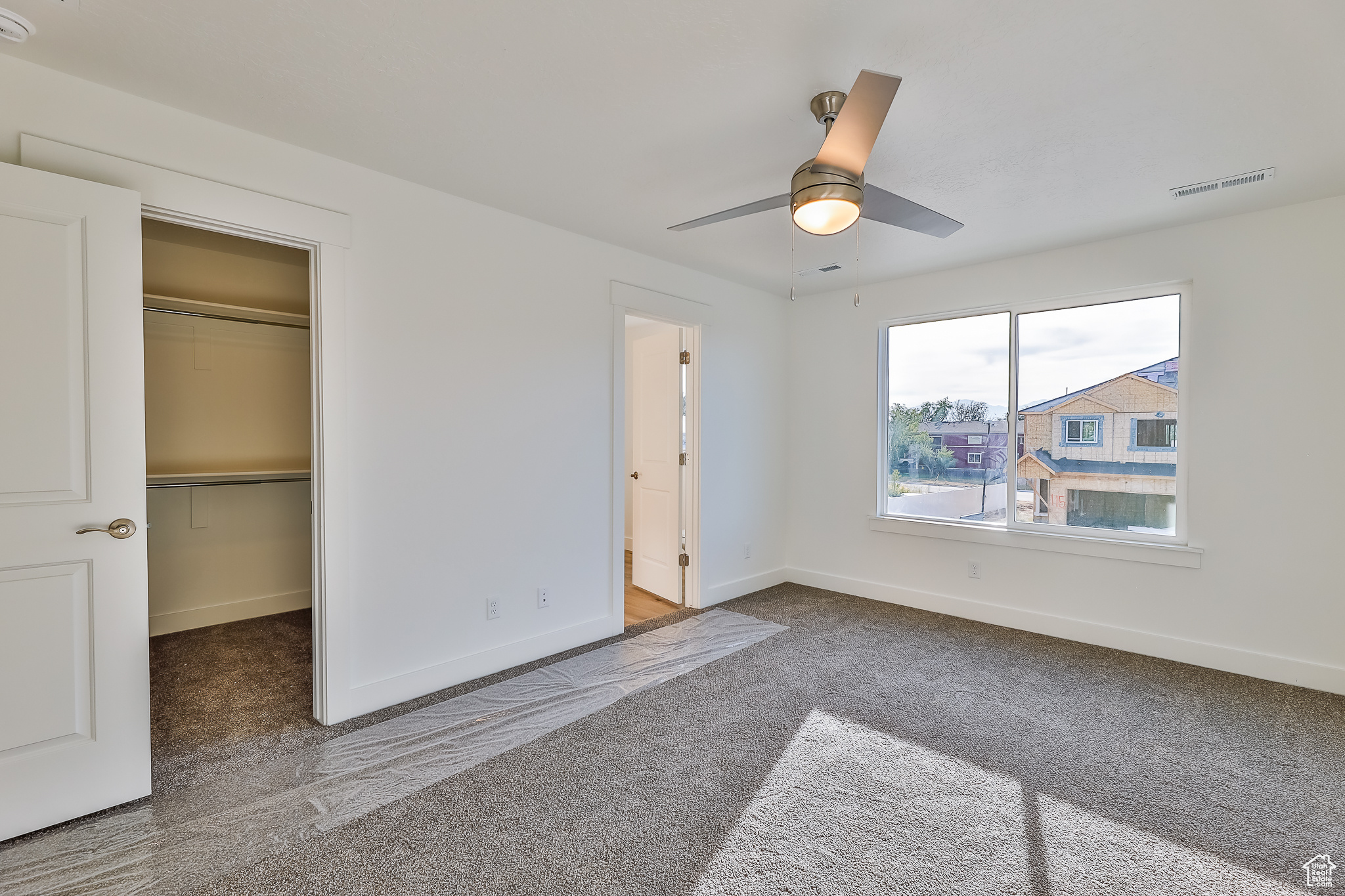 Unfurnished bedroom featuring dark colored carpet, a spacious closet, ceiling fan, and a closet