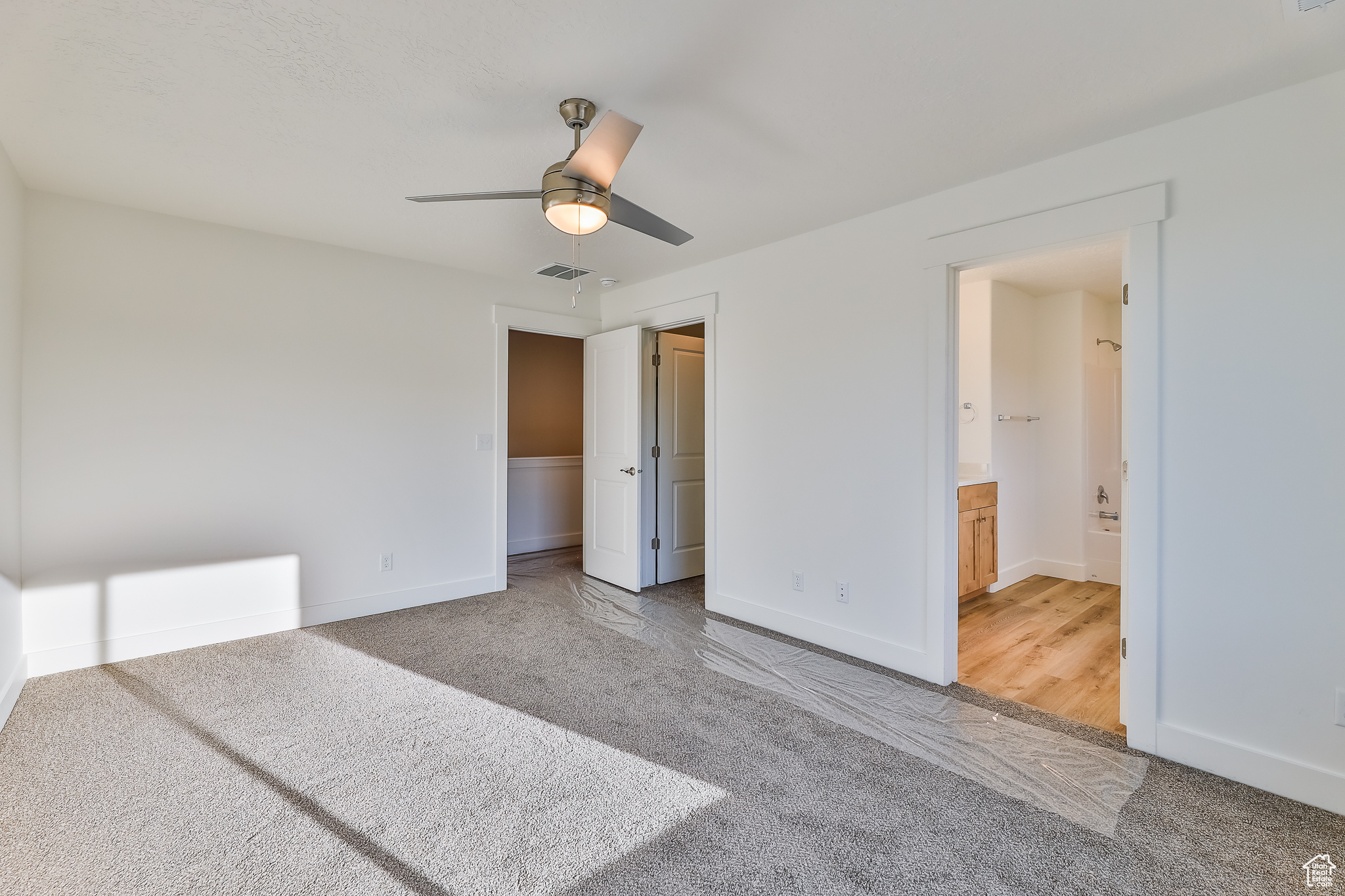 Unfurnished bedroom with connected bathroom, ceiling fan, and carpet