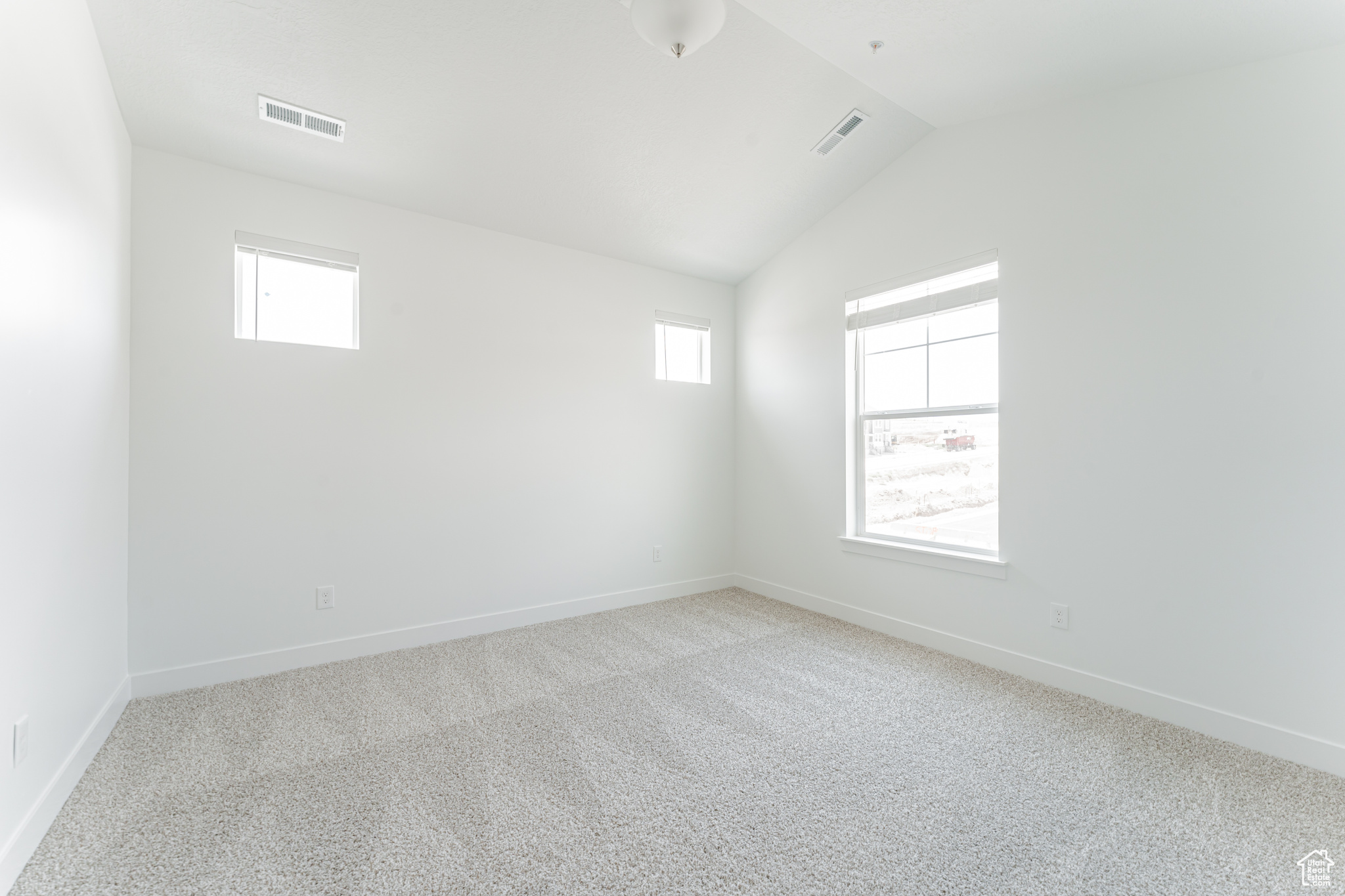 Carpeted spare room featuring lofted ceiling and a healthy amount of sunlight