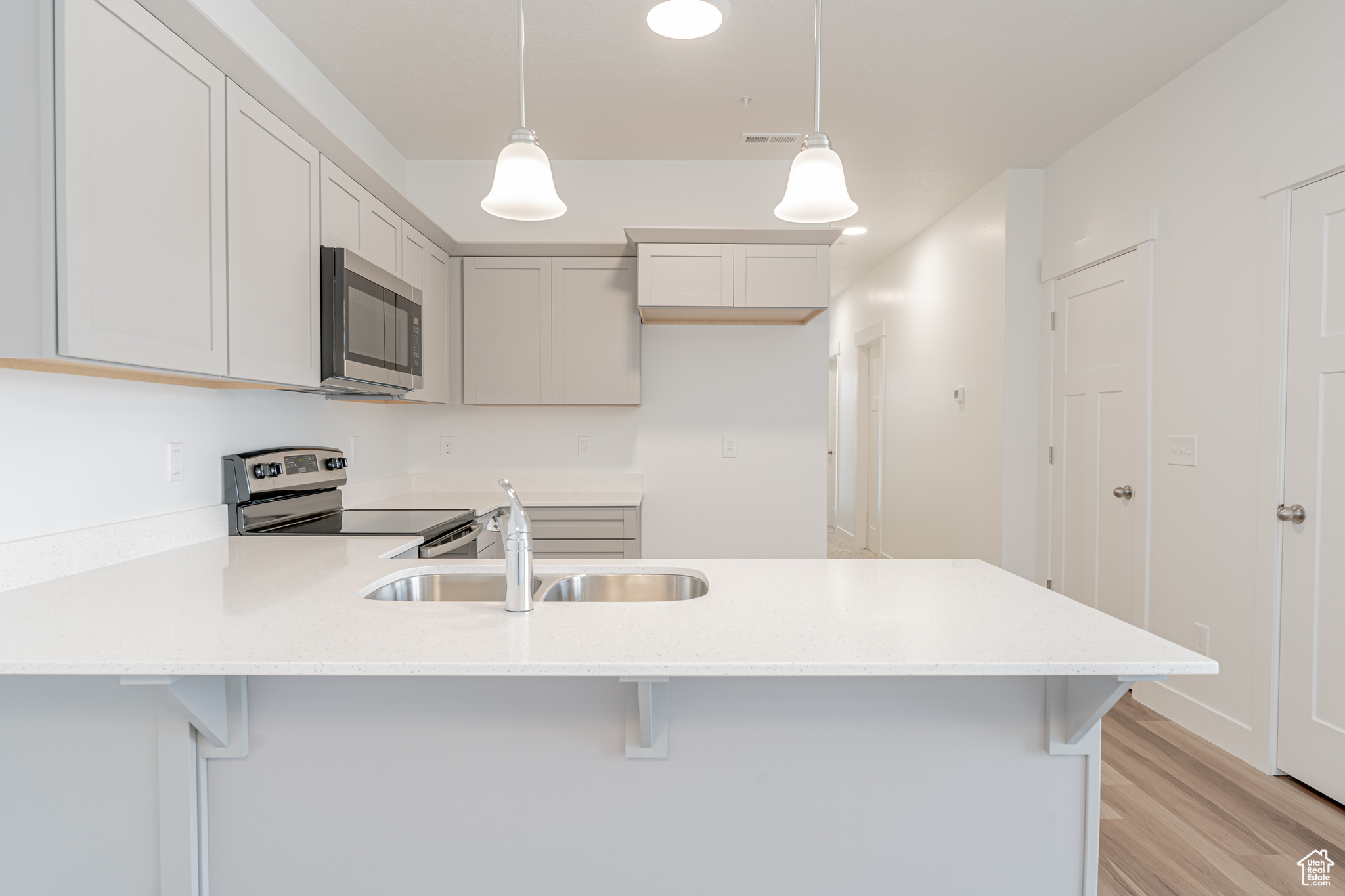 Kitchen featuring a breakfast bar area, appliances with stainless steel finishes, hanging light fixtures, light hardwood / wood-style floors, and sink