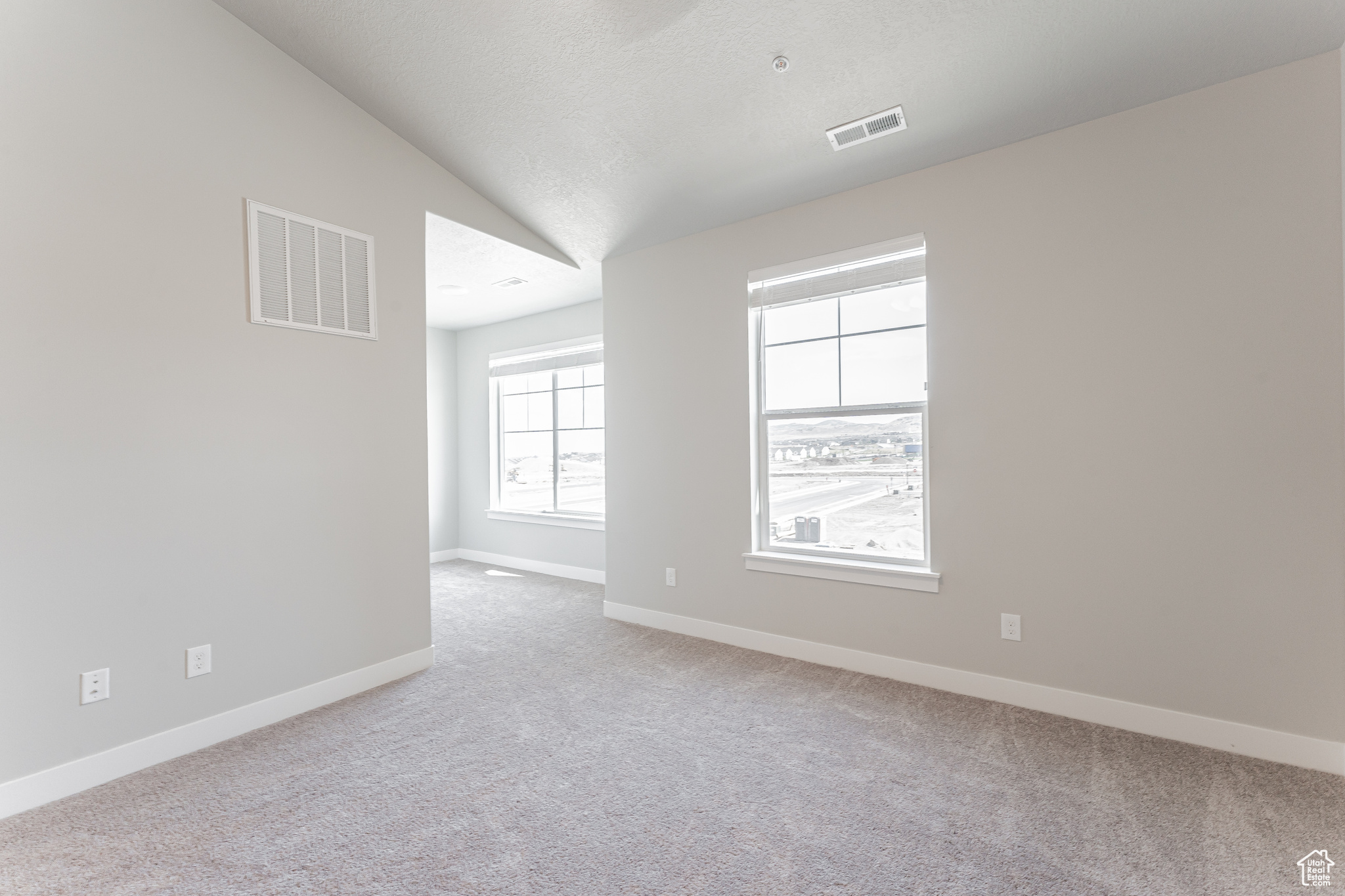 Empty room with a textured ceiling, light carpet, and vaulted ceiling