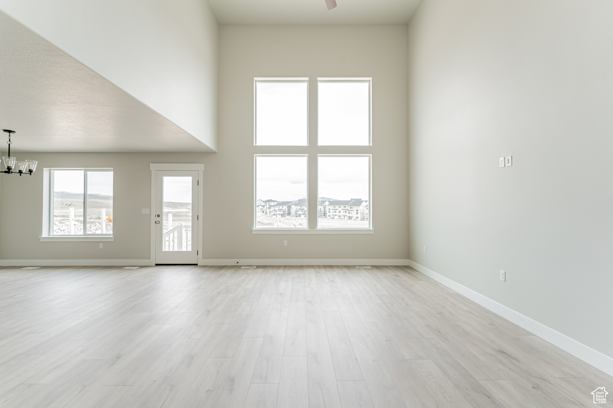 Spare room with ceiling fan with notable chandelier, light wood-type flooring, and a high ceiling