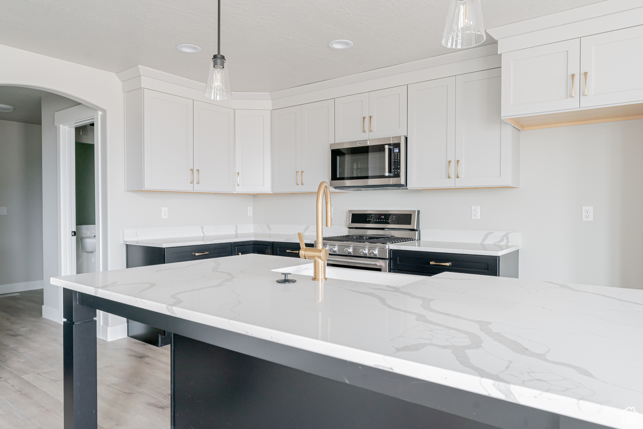 Kitchen featuring light hardwood / wood-style flooring, stainless steel appliances, white cabinets, and light stone counters