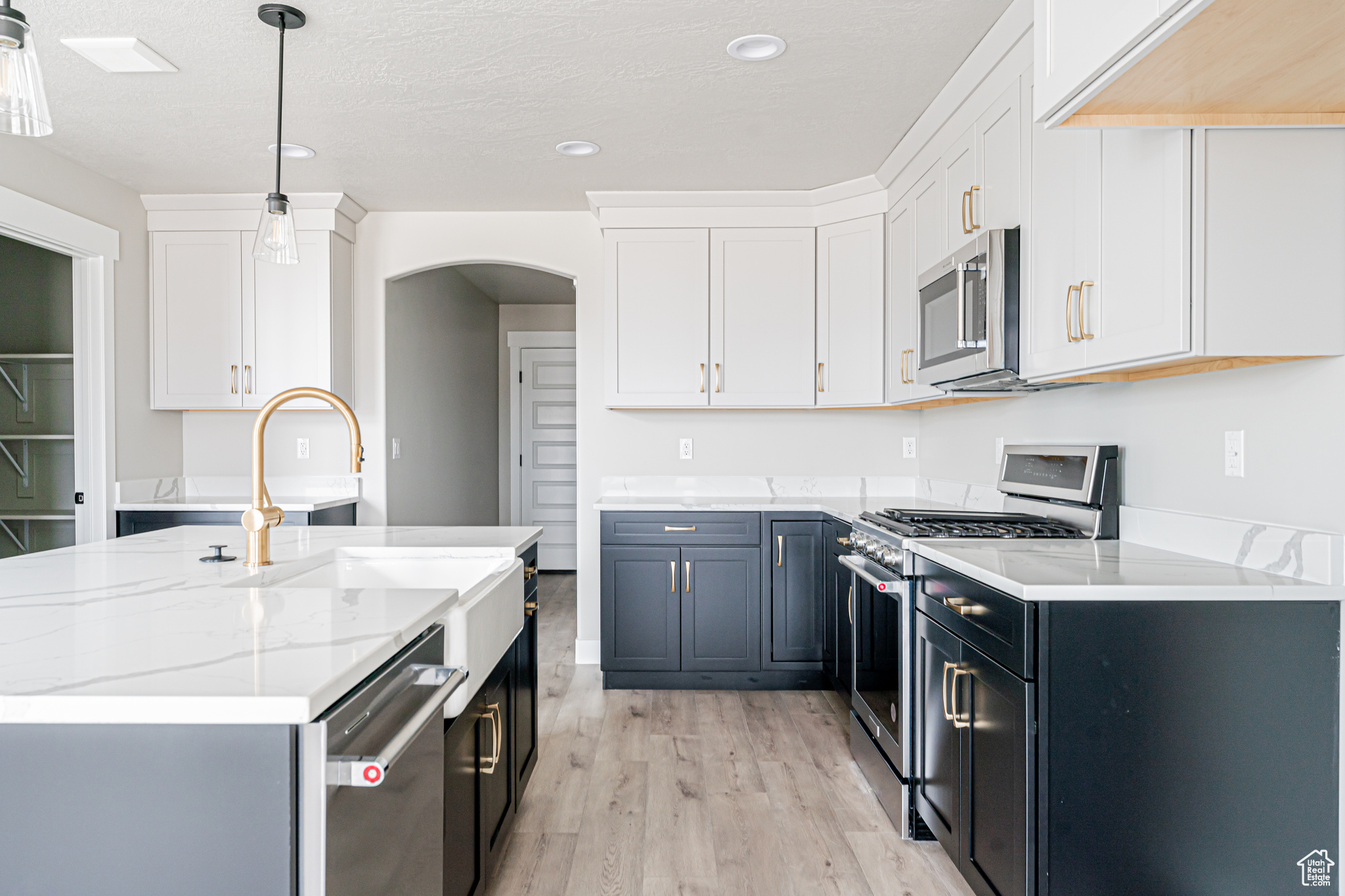 Kitchen with light hardwood / wood-style flooring, appliances with stainless steel finishes, white cabinets, hanging light fixtures, and light stone counters