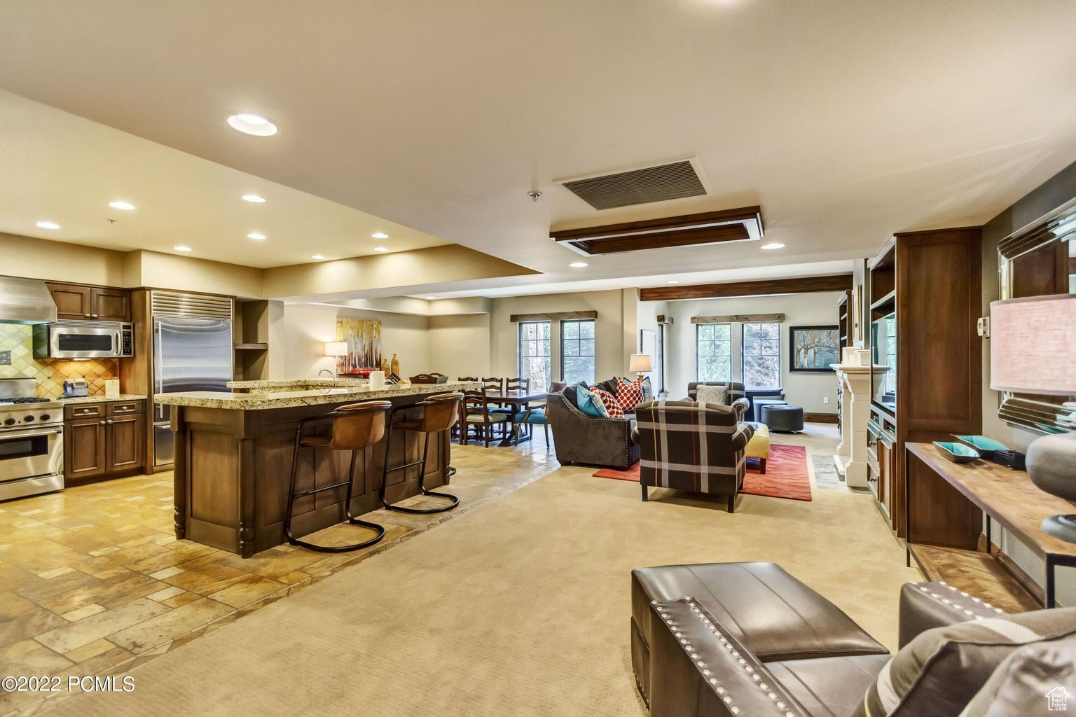 Kitchen with backsplash, a kitchen breakfast bar, light stone countertops, appliances with stainless steel finishes, and wall chimney exhaust hood