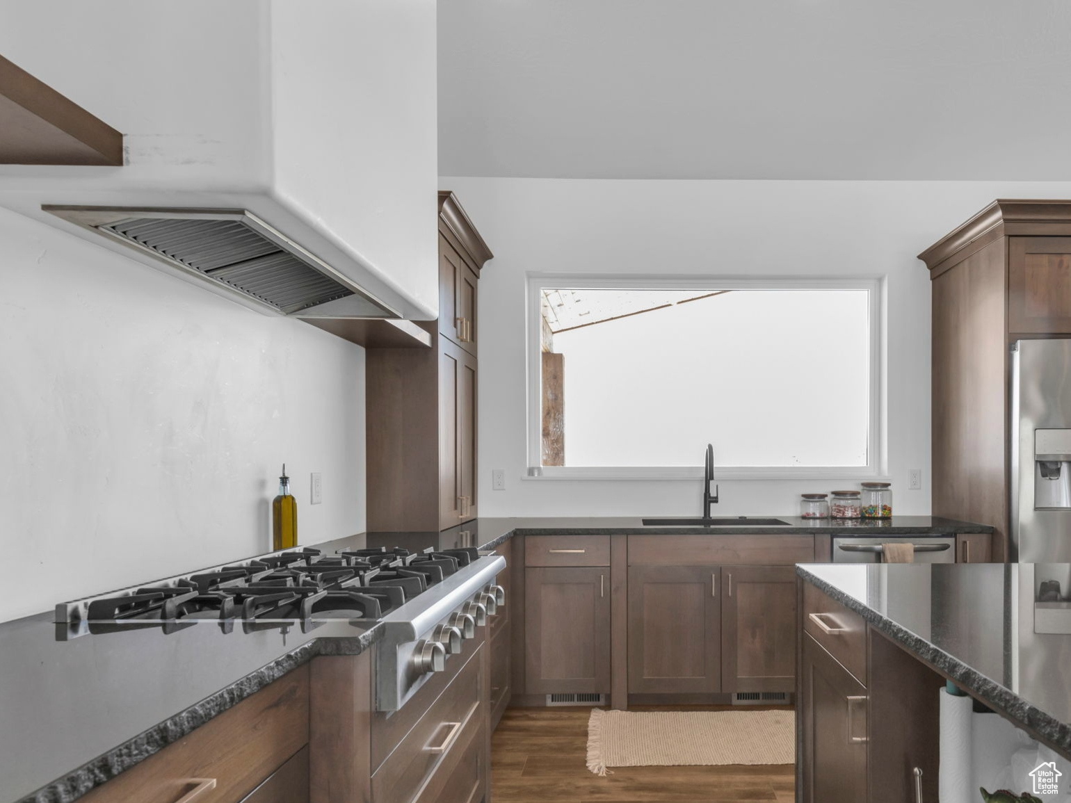 Kitchen with dark brown cabinets, dark hardwood / wood-style flooring, sink, stainless steel fridge with ice dispenser, and dark stone countertops