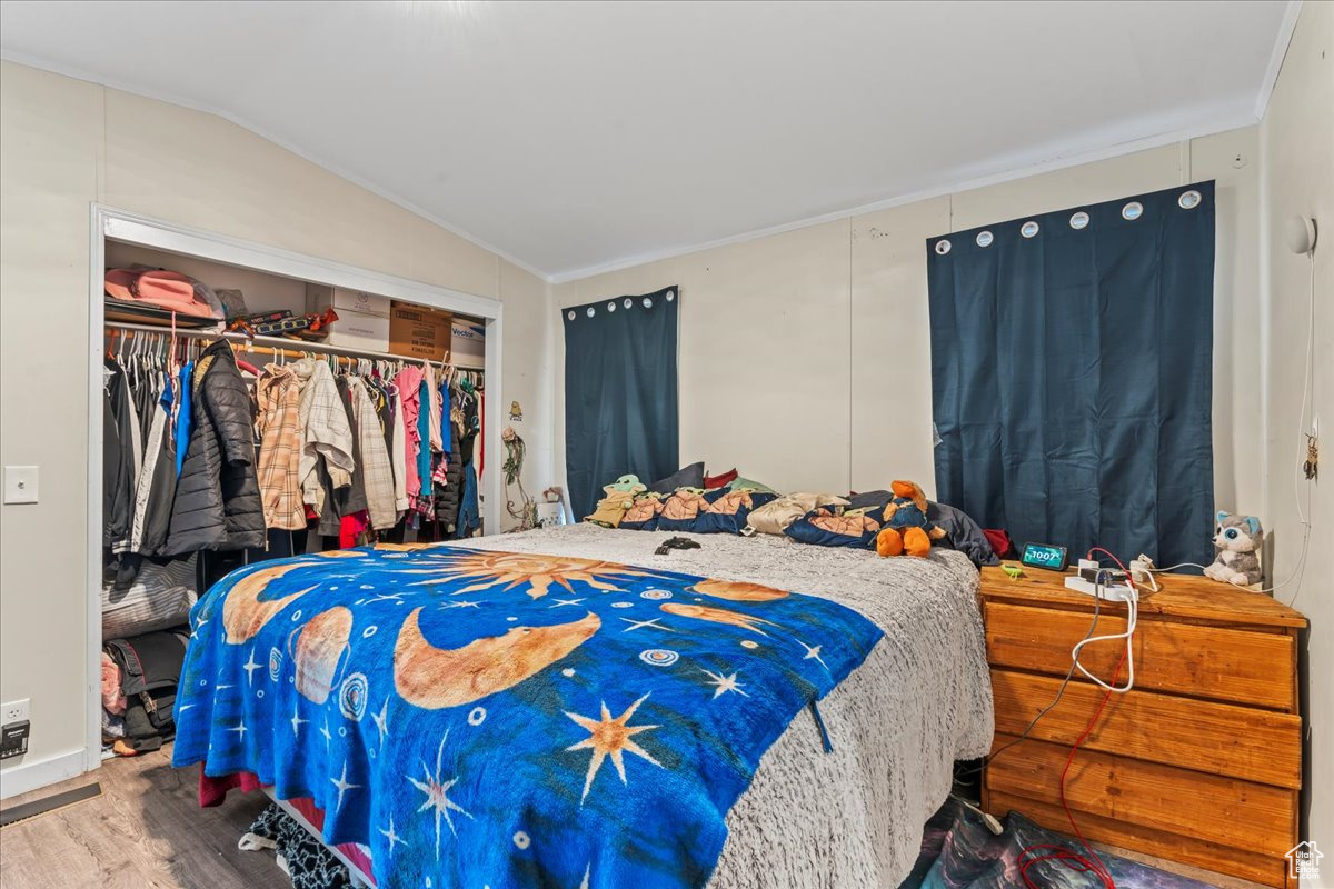 Bedroom with a closet, ornamental molding, vaulted ceiling, and wood-type flooring