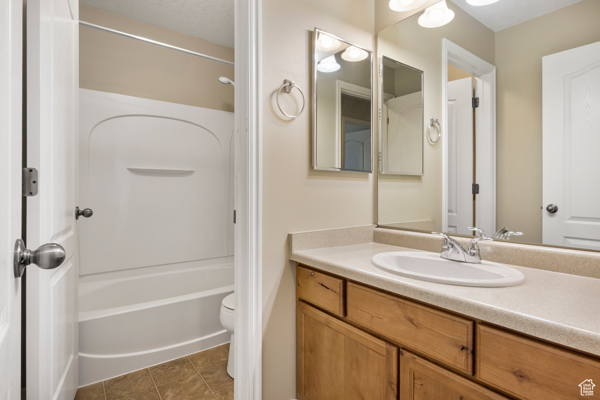 Full bathroom with shower / washtub combination, tile floors, vanity with extensive cabinet space, and toilet
