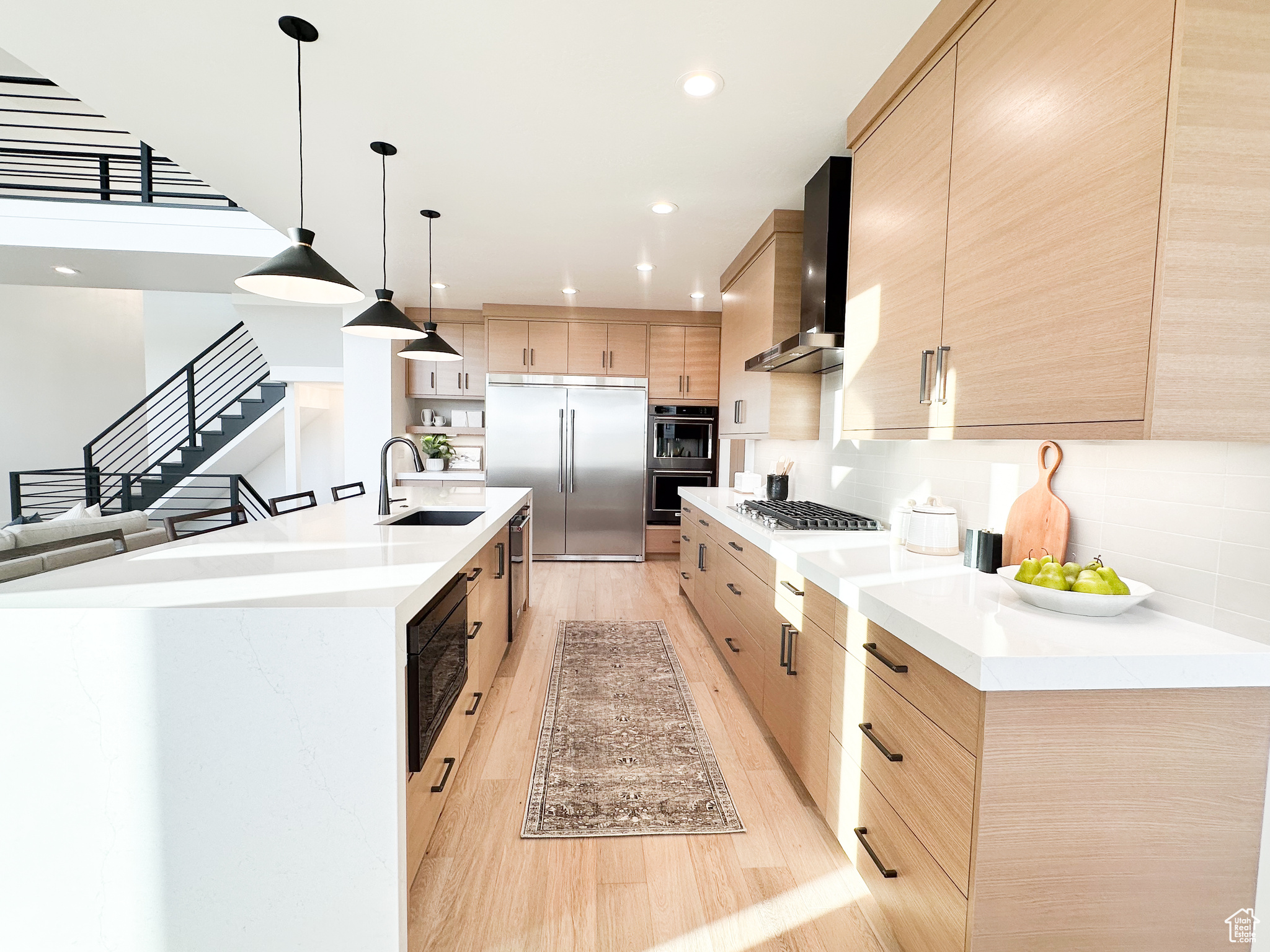 Kitchen with wall chimney range hood, light hardwood / wood-style flooring, tasteful backsplash, built in appliances, and sink