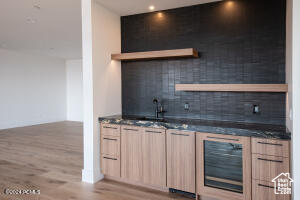 Bar with light brown cabinetry, sink, wood-type flooring, and decorative backsplash