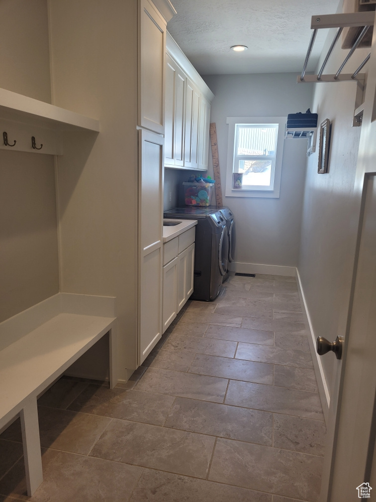 Clothes washing area featuring cabinets, washer and clothes dryer, and tile flooring
