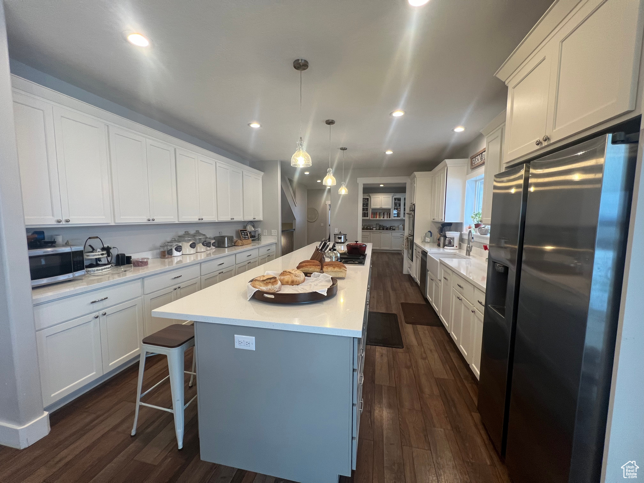 Kitchen featuring white cabinets, appliances with stainless steel finishes, an island with sink, dark hardwood / wood-style floors, and decorative light fixtures