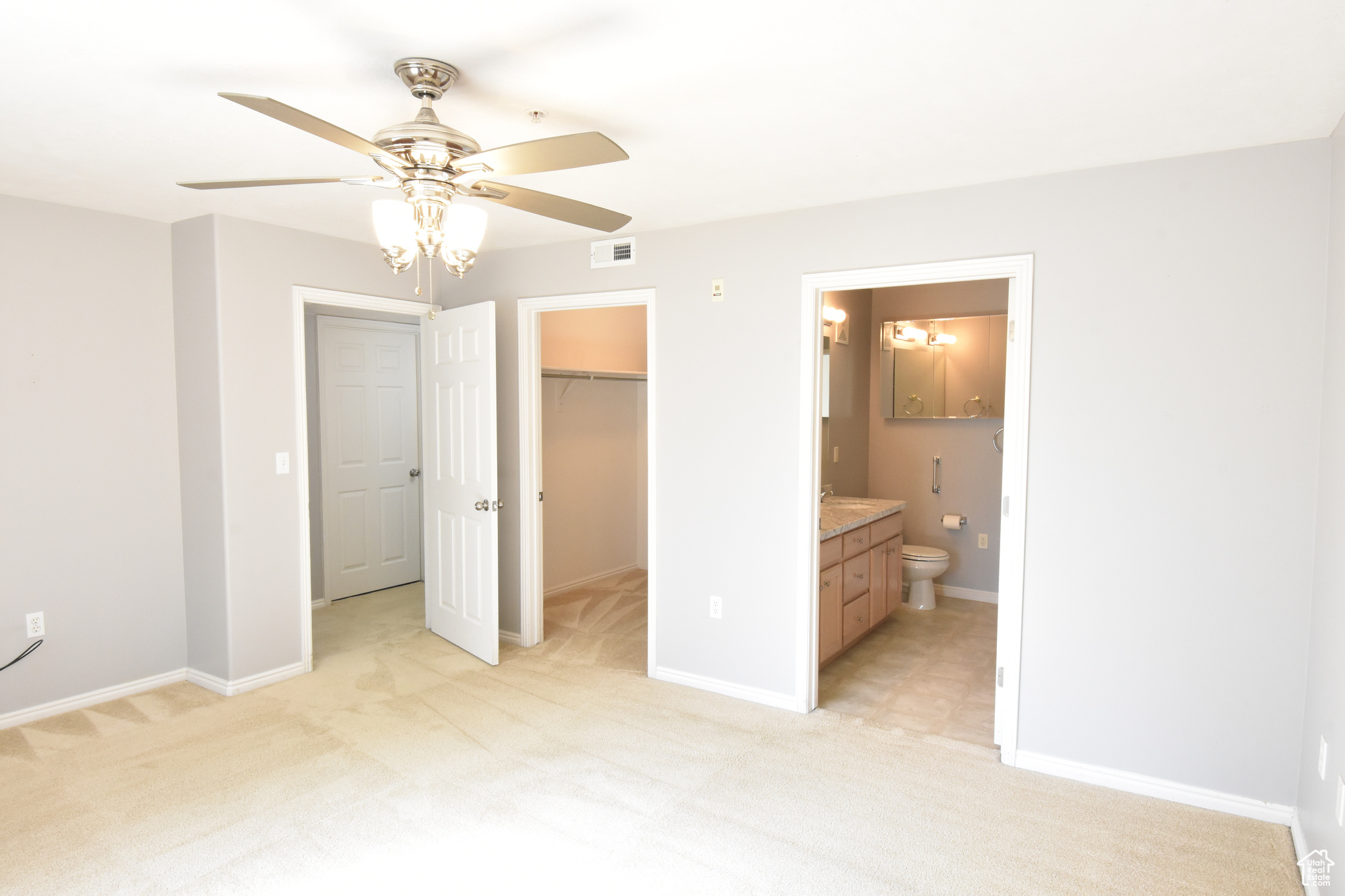 Unfurnished bedroom featuring ceiling fan, a closet, ensuite bathroom, light colored carpet, and a walk in closet