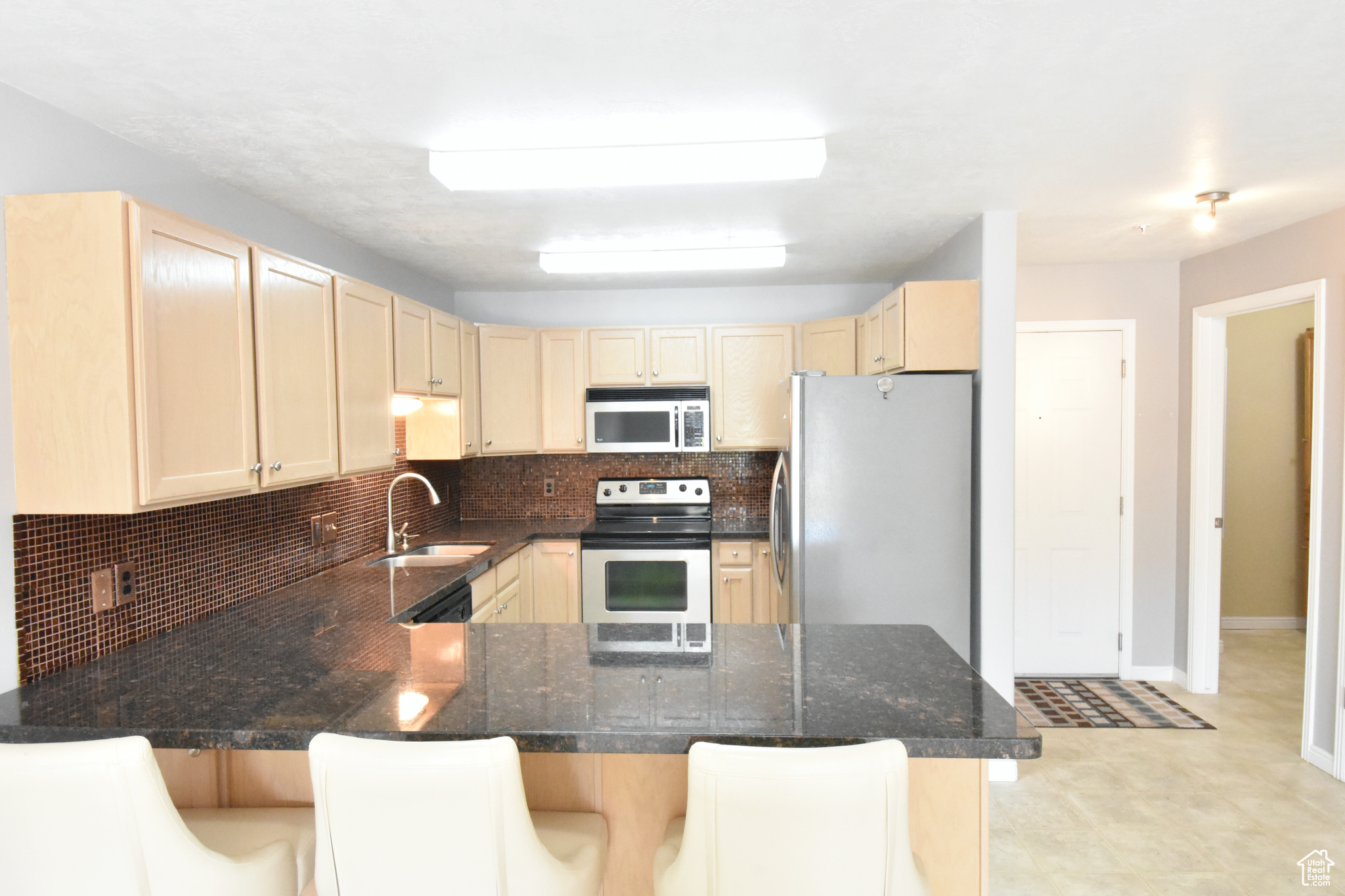 Kitchen with appliances with stainless steel finishes, a breakfast bar area, kitchen peninsula, tasteful backsplash, and light tile floors