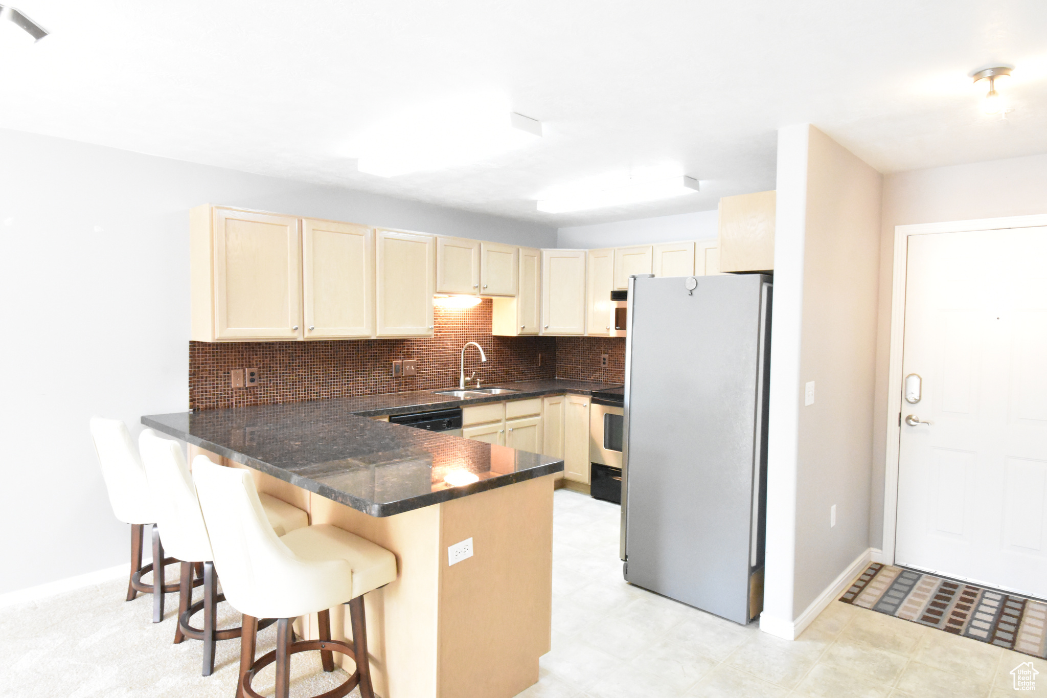 Kitchen featuring stainless steel refrigerator, kitchen peninsula, a kitchen bar, sink, and light tile floors