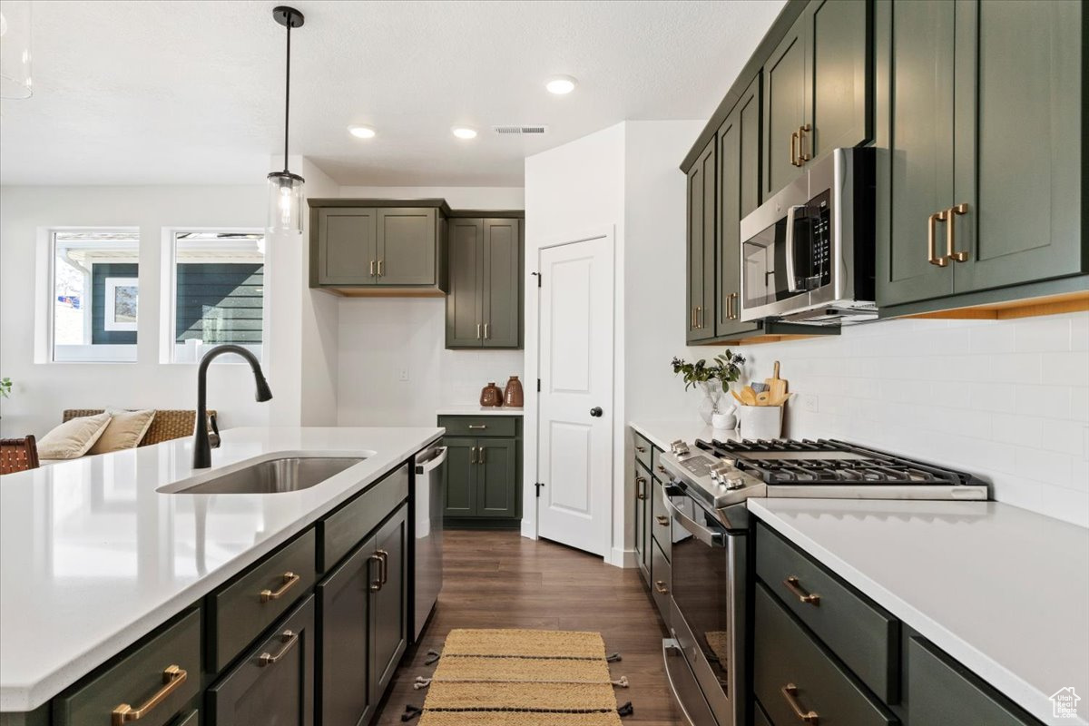 Kitchen featuring decorative light fixtures, stainless steel appliances, tasteful backsplash, dark wood-type flooring, and sink