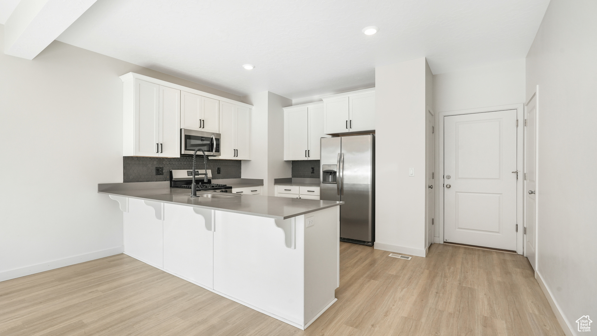 Kitchen with stainless steel appliances, white cabinetry, kitchen peninsula, light hardwood / wood-style floors, and a kitchen breakfast bar