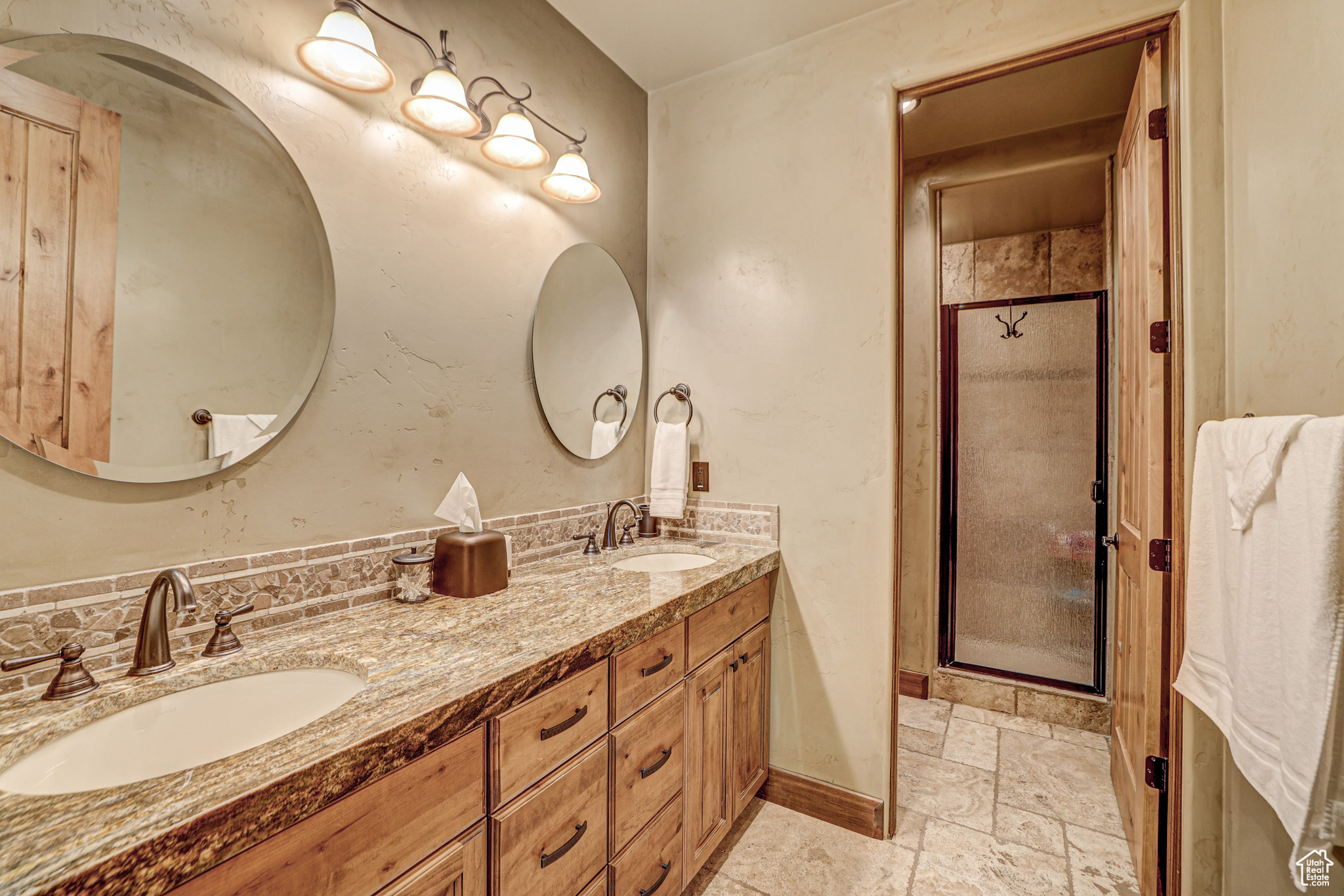 Bathroom with dual sinks, backsplash, vanity with extensive cabinet space, an enclosed shower, and tile floors