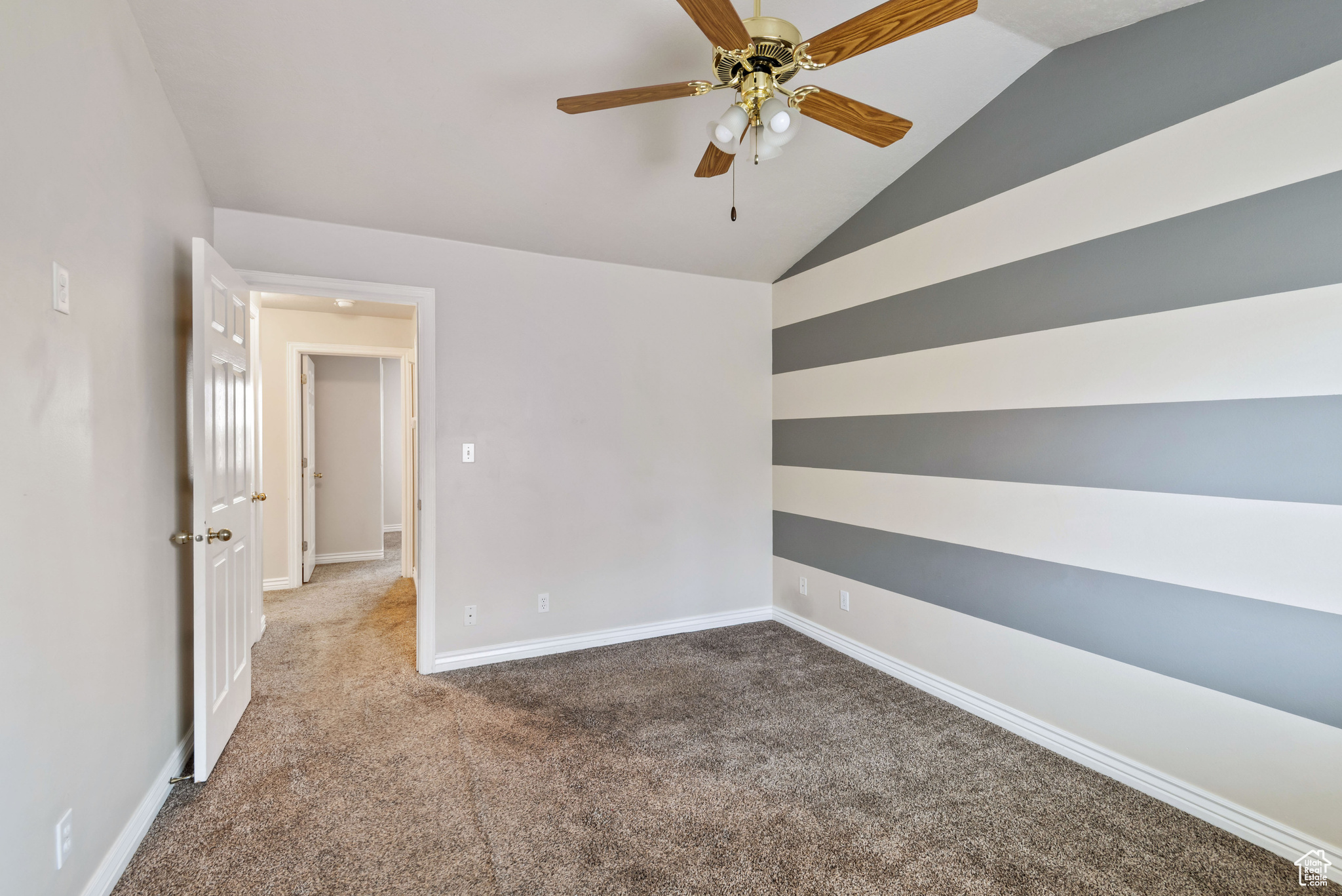 Empty room featuring dark carpet, ceiling fan, and lofted ceiling