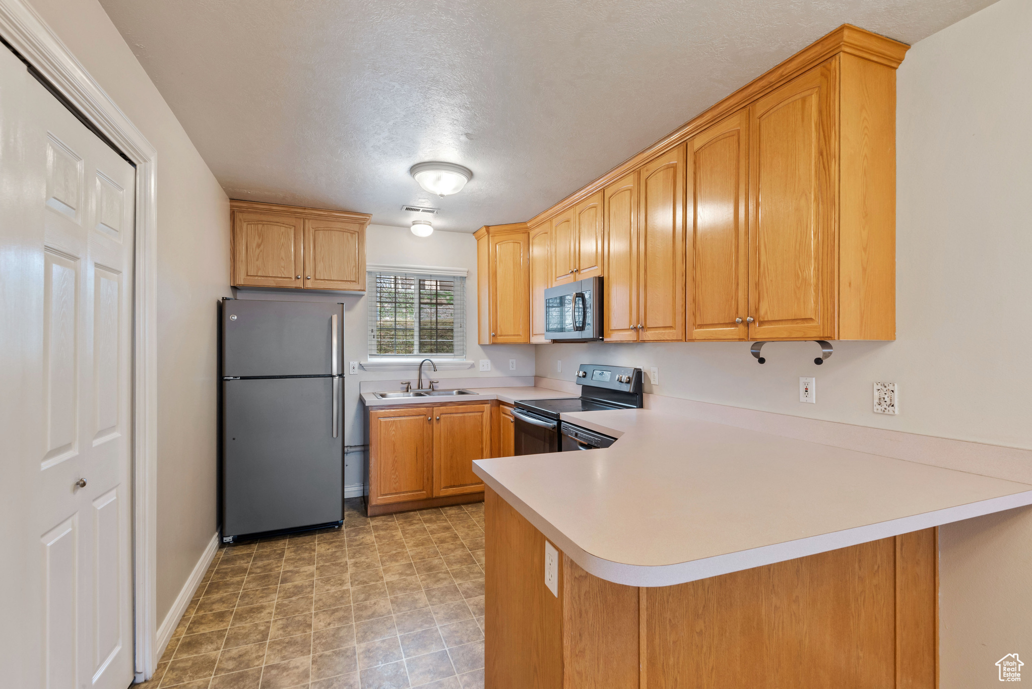 Kitchen featuring sink, stainless steel appliances, light tile flooring, and kitchen peninsula